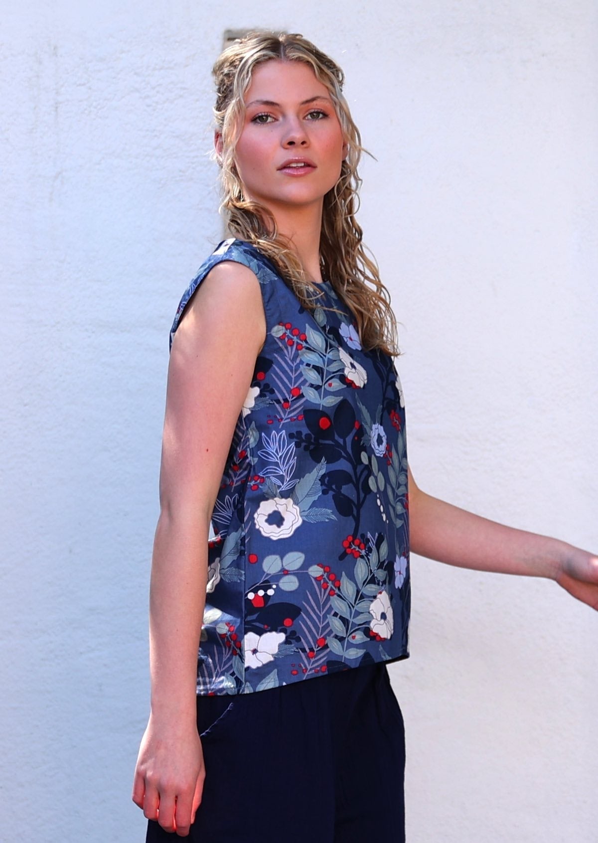 Model standing in front of white wall wearing 100 percent cotton navy blue floral with pops of red, sleeveless top