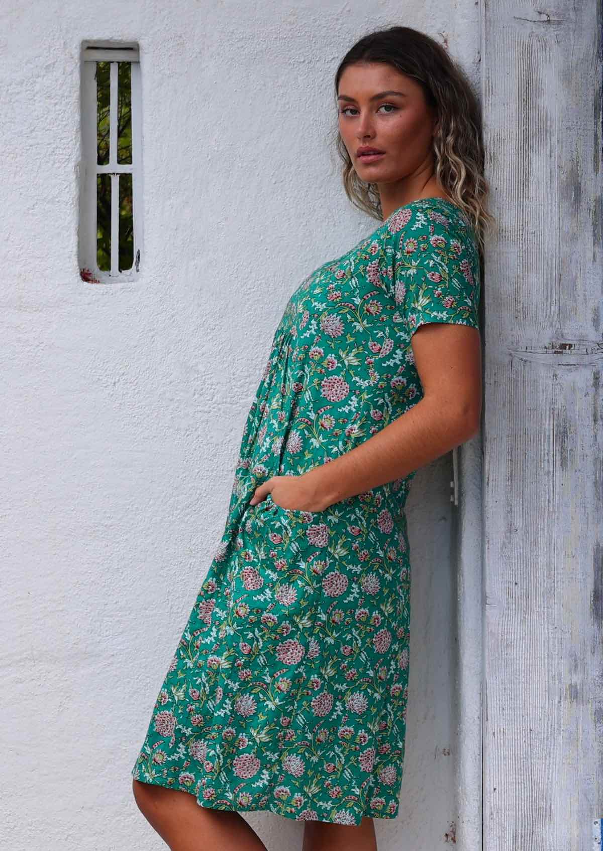 Model leaning on wooden post with hand in pocket wearing 100 percent cotton green sundress