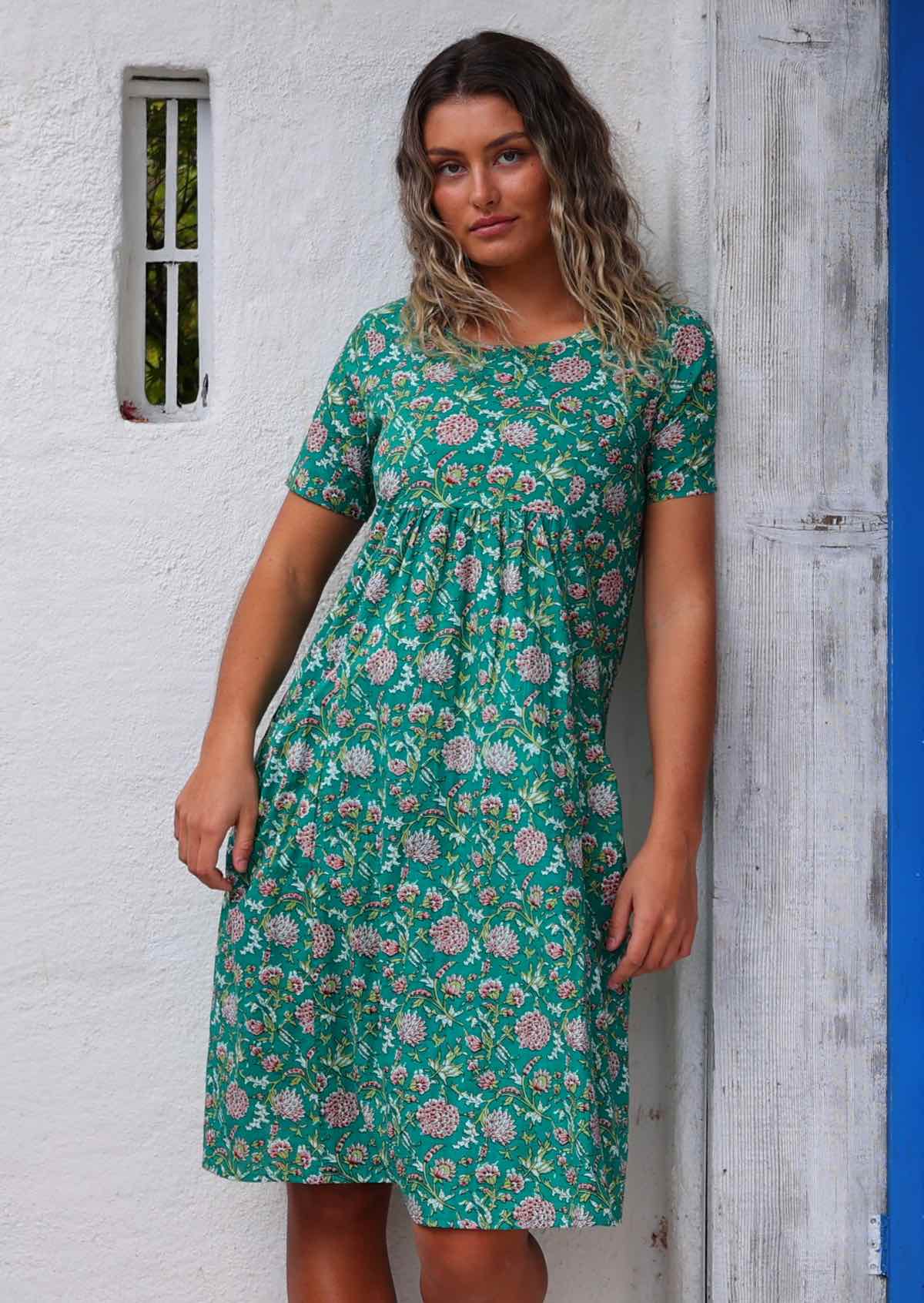 Model leaning on wooden post wearing 100 percent cotton green sundress