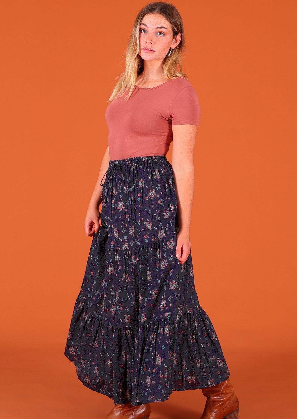 Model standing side on wearing dark Purple 100 percent cotton Indian floral printed three tiered maxi skirt