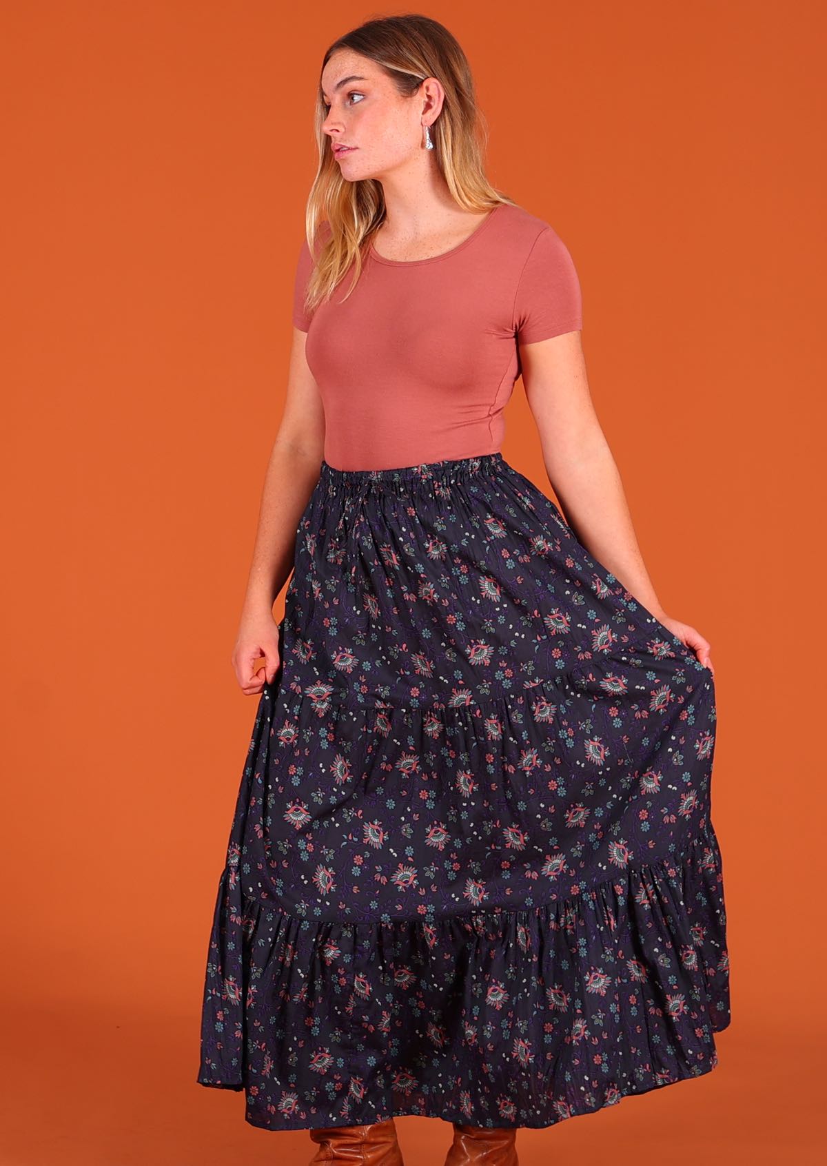 Model standing holding middle tier of dark Purple 100 percent cotton Indian floral printed three tiered maxi skirt