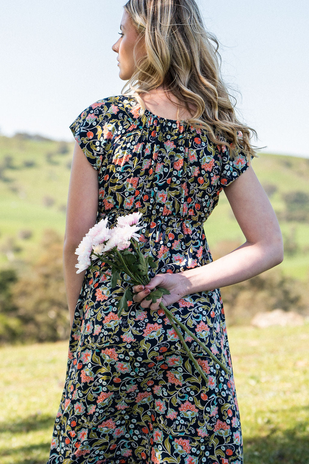Back view of model holding flowers wearing 100 percent rayon floral maxi dress