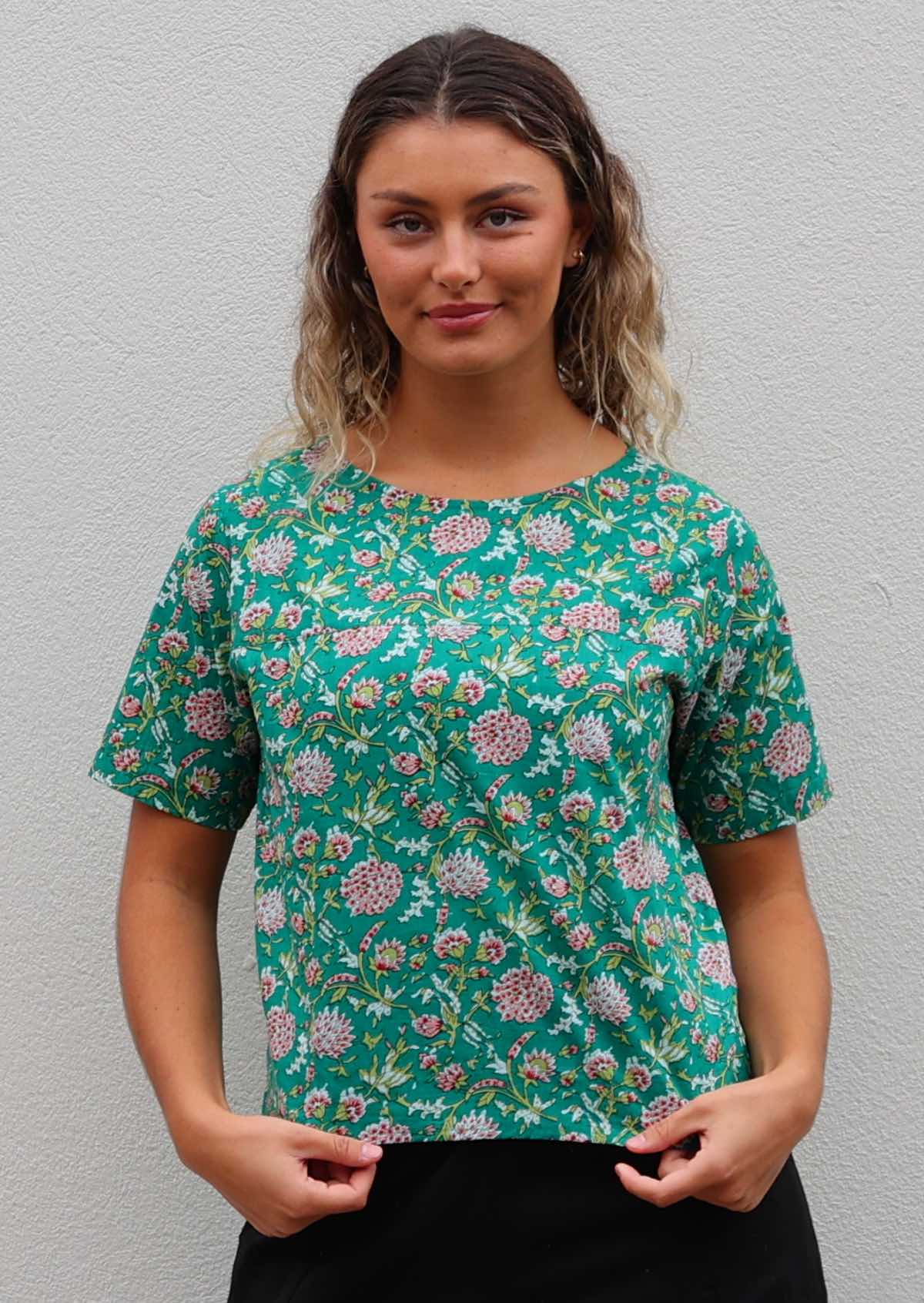 Model poses in 100% cotton short sleeve top with high round neckline, in floral print on jade green base