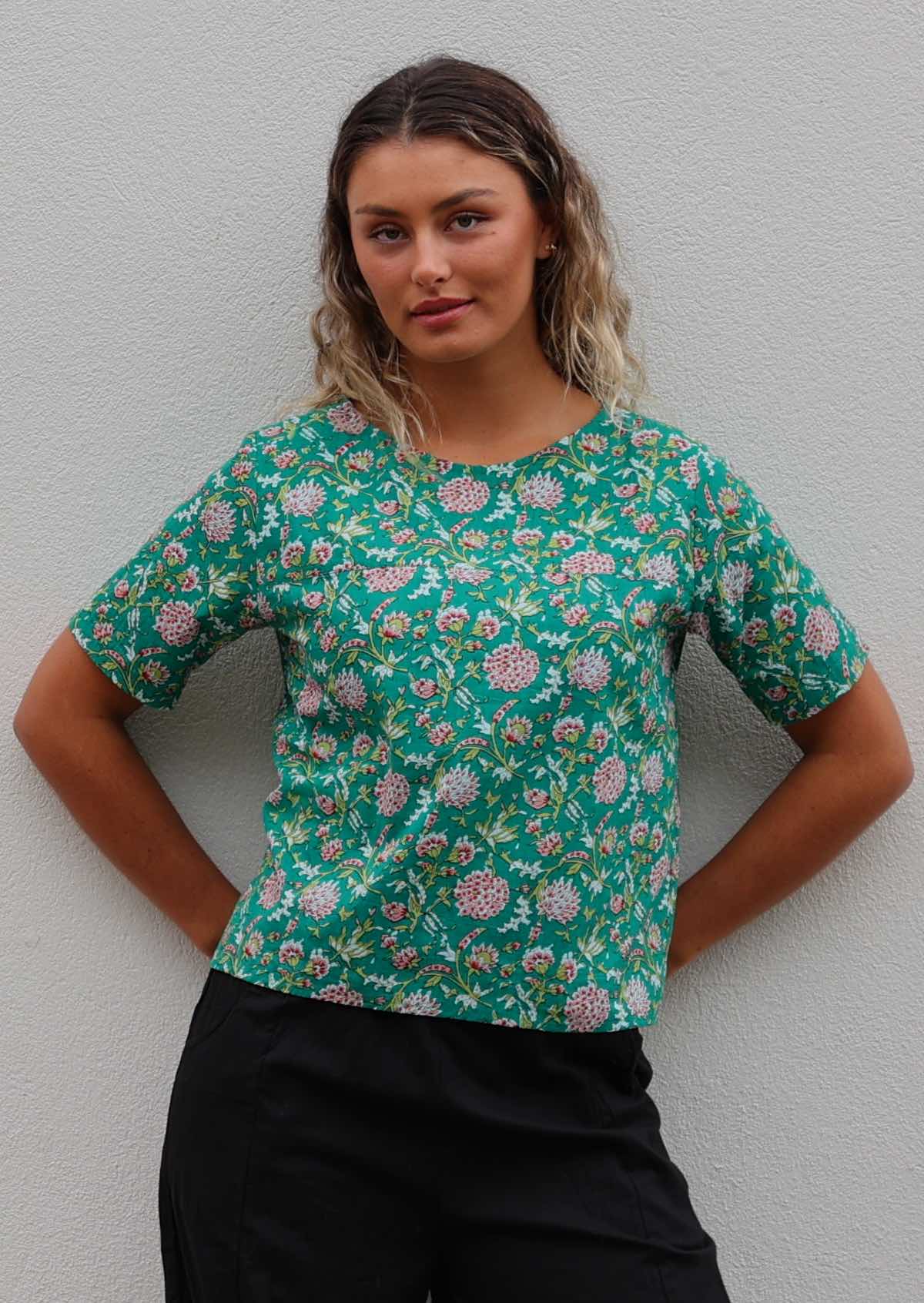 Woman leans on wall in cotton relaxed fit floral top with T-shirt sleeves and high round neckline