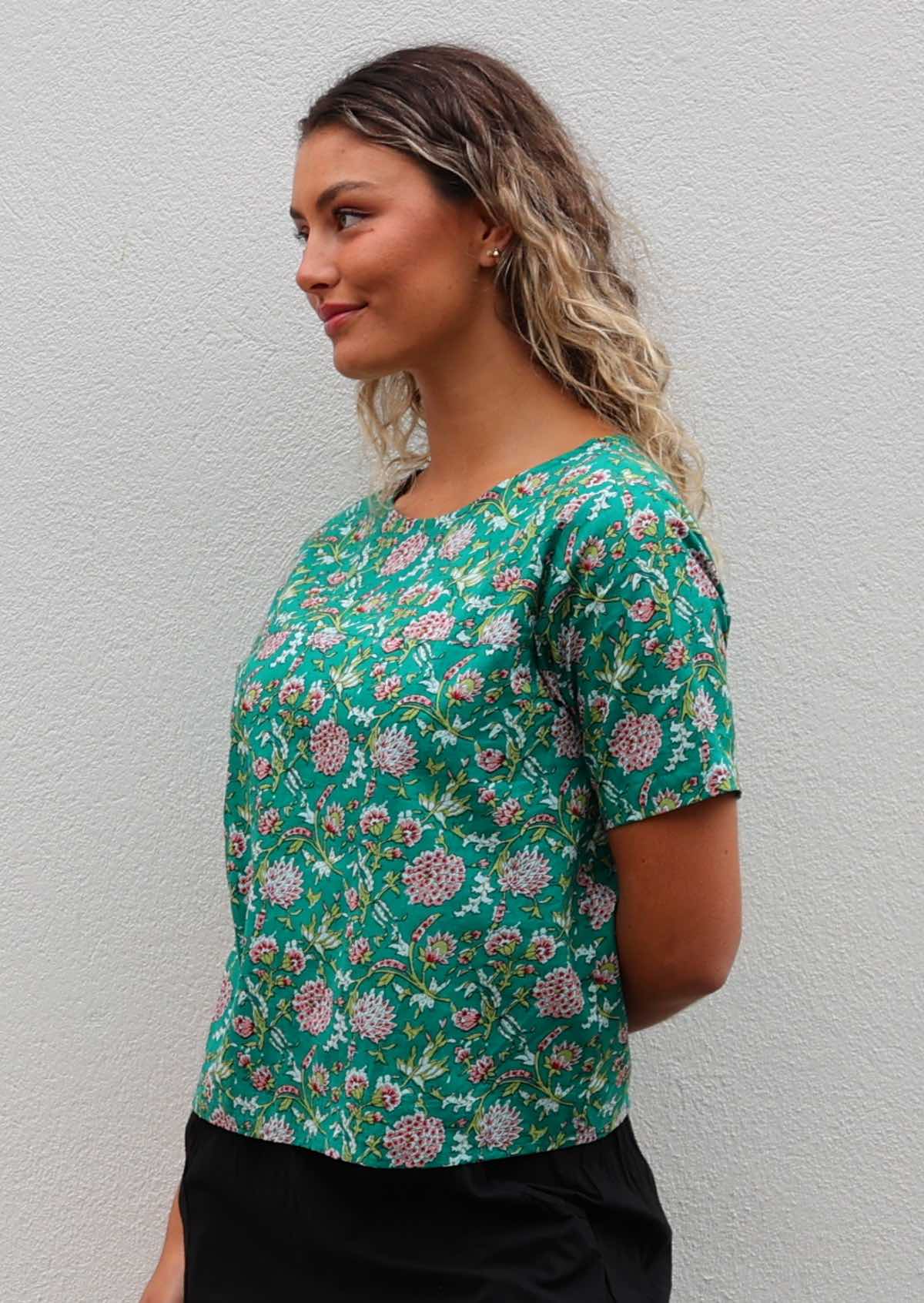 Woman looks to the side in cotton jade green based floral print short sleeved top with high round neckline