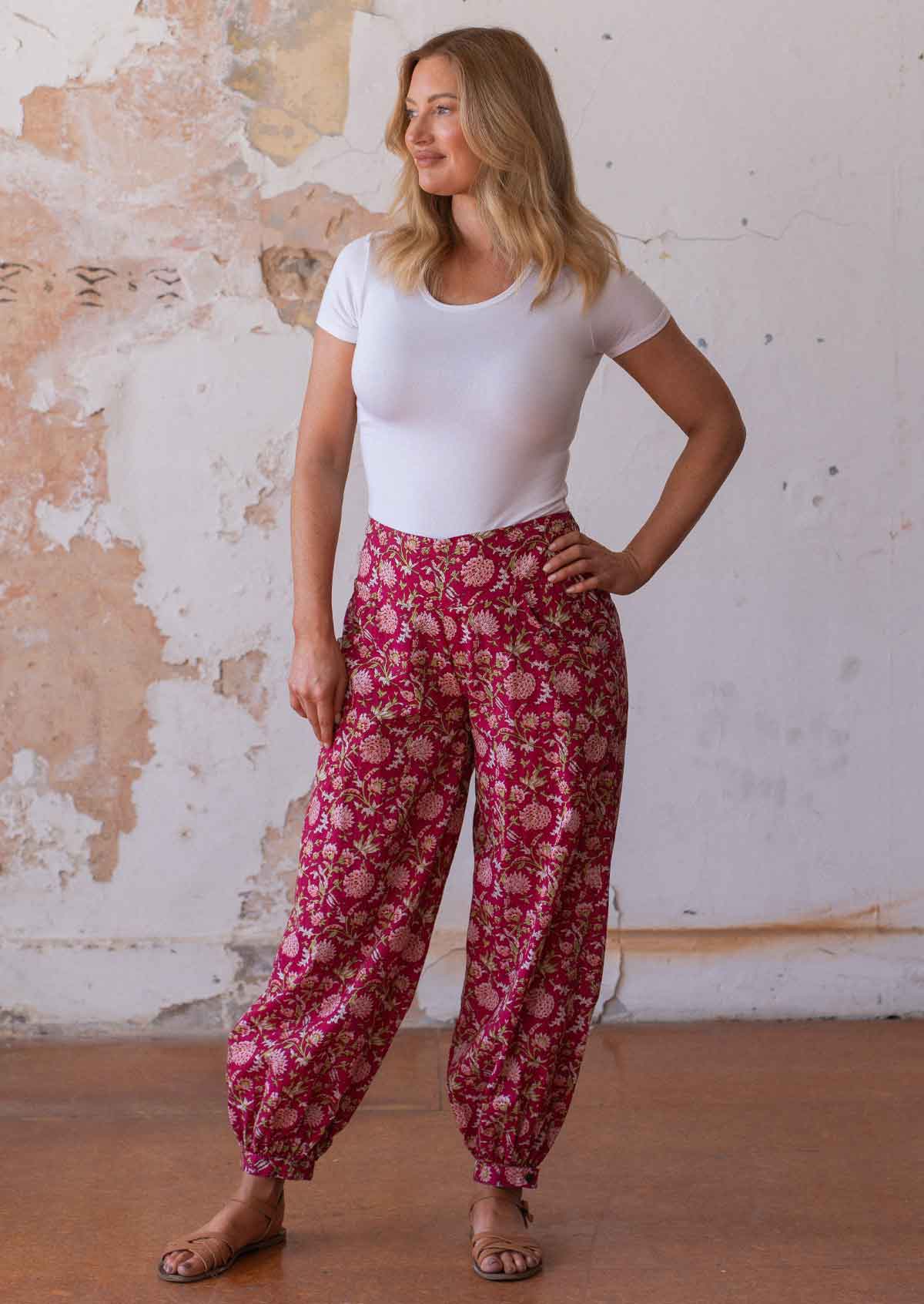 Woman poses with hand on ྀིྀི in floral print on red base cotton harem pants with white stretch rayon top