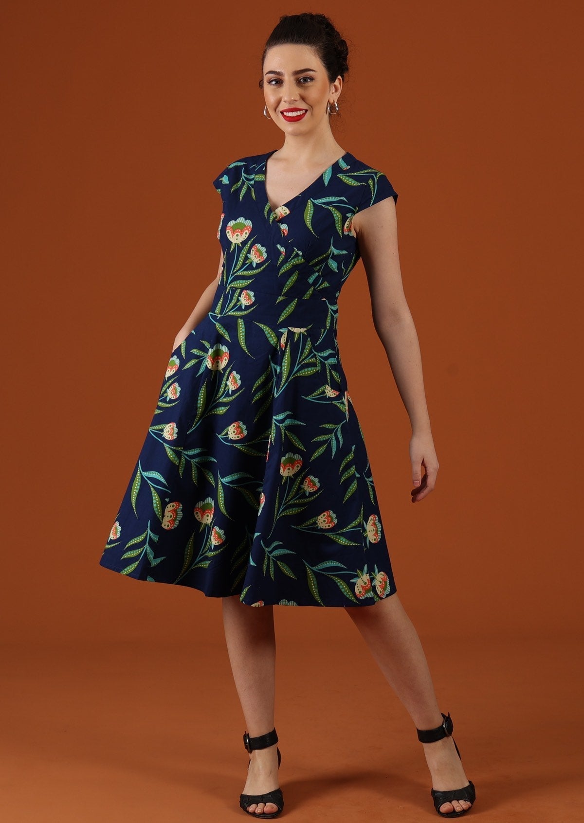 Model wears floral print dress on navy base. 