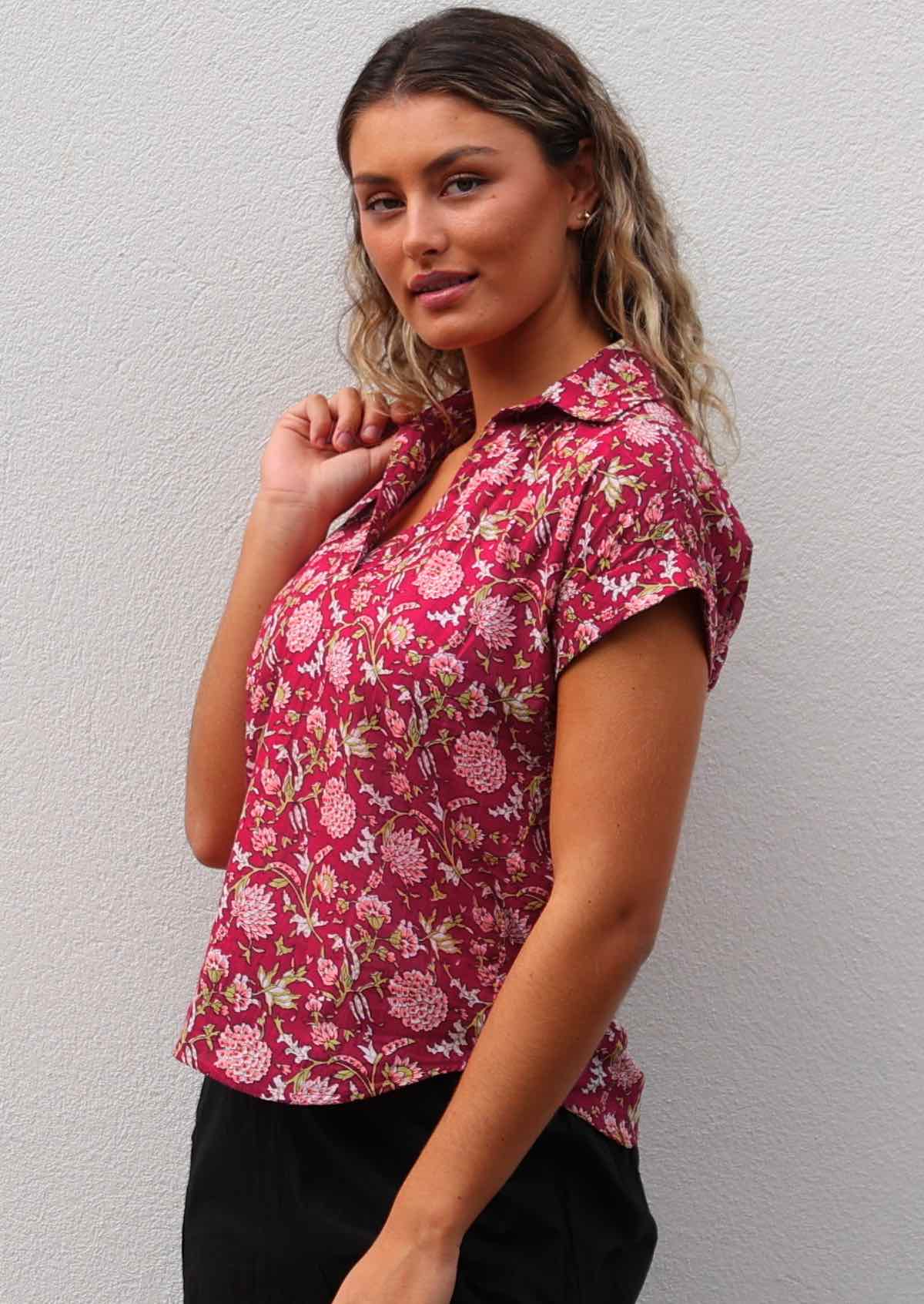 Woman wears cotton short sleeve shirt with V-neckline and collar in a floral print on a bright red base