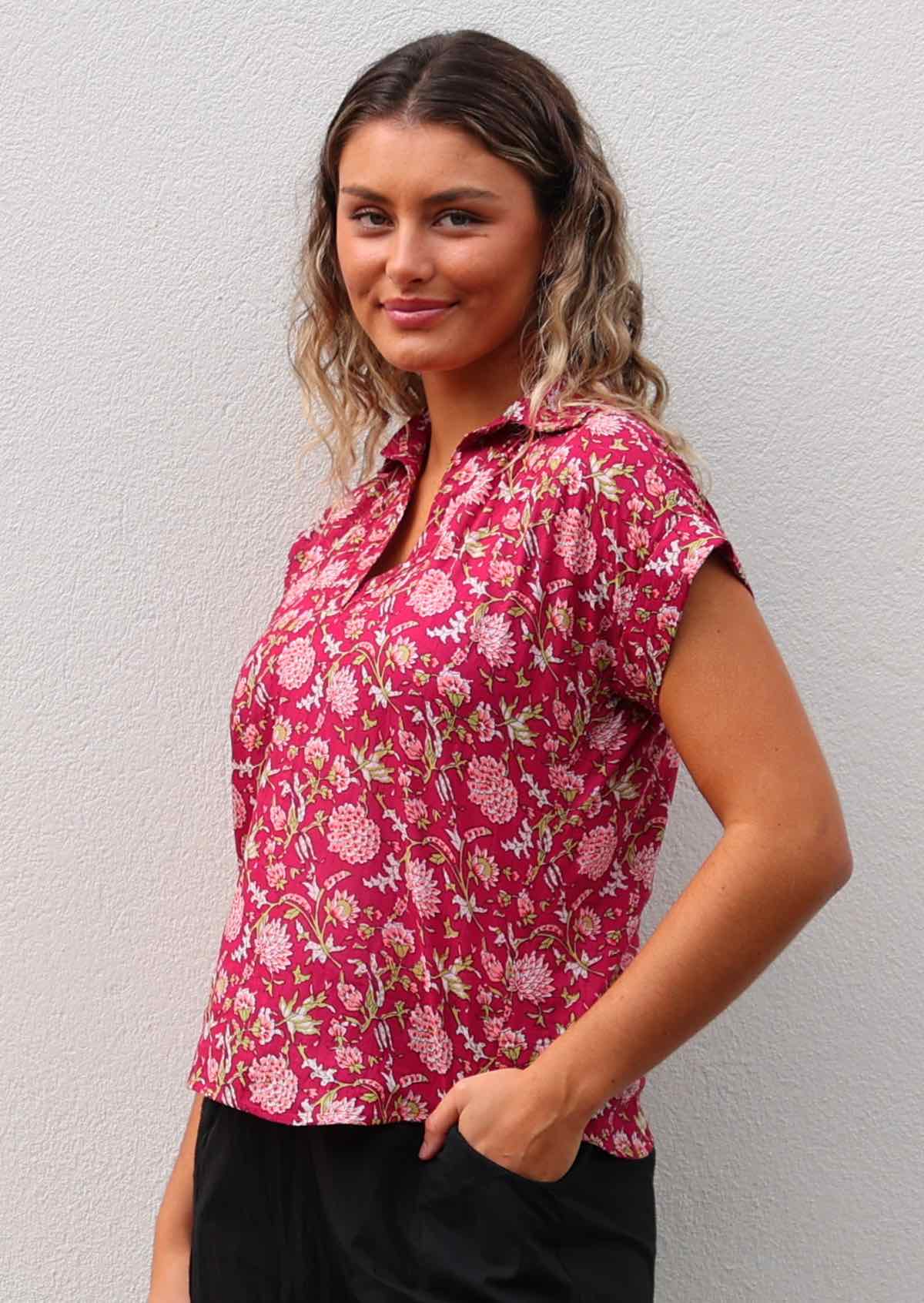 Model poses in cotton relaxed fit short sleeve top with collar, in floral print on bright red base