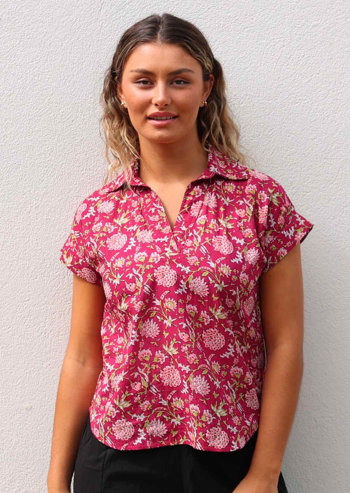 Woman wears cotton short sleeve top with V-neckline and collar in floral print on a red base