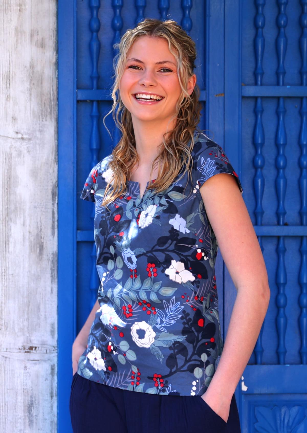 Woman smiles in bold blue floral print cotton top with hands in pockets of pants