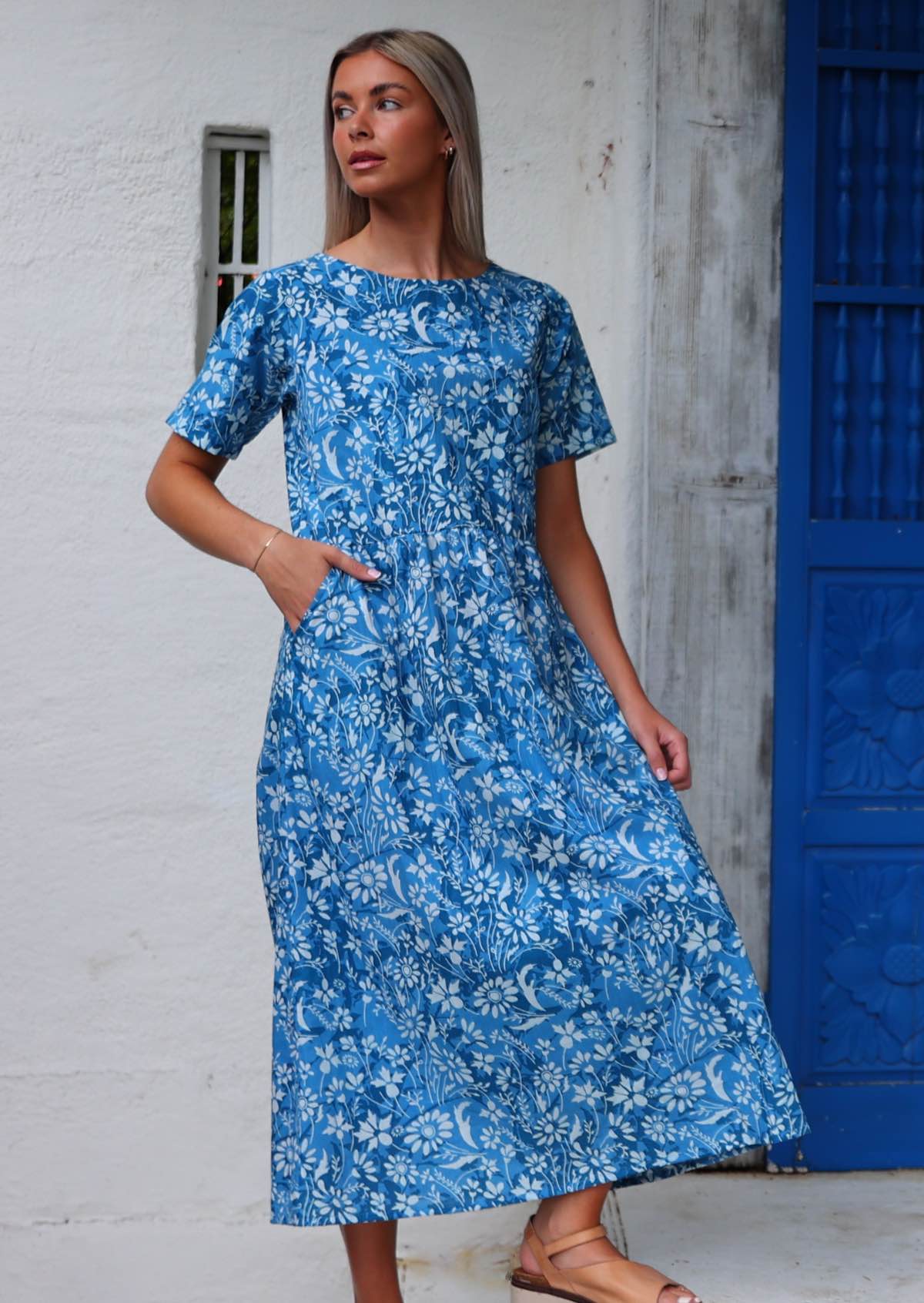 Woman stands on steps in cotton midi length relaxed fit dress with hand in pocket