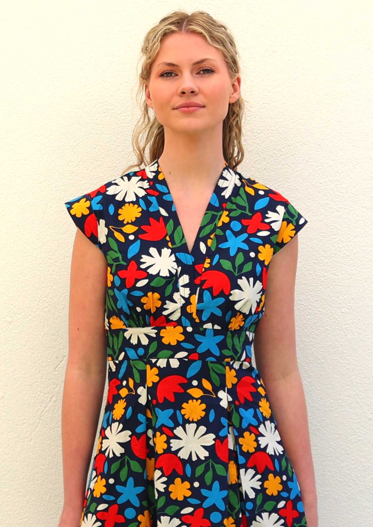 Close up of Model wearing 100 percent cotton dark navy blue base and bright abstract floral print cotton retro dress with modest V-neckline and box pleats at the waist