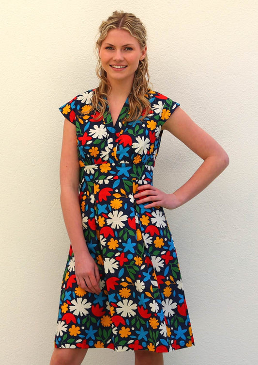 Model with one hand on hip wearing 100 percent cotton dark navy blue base and bright abstract floral print cotton retro dress