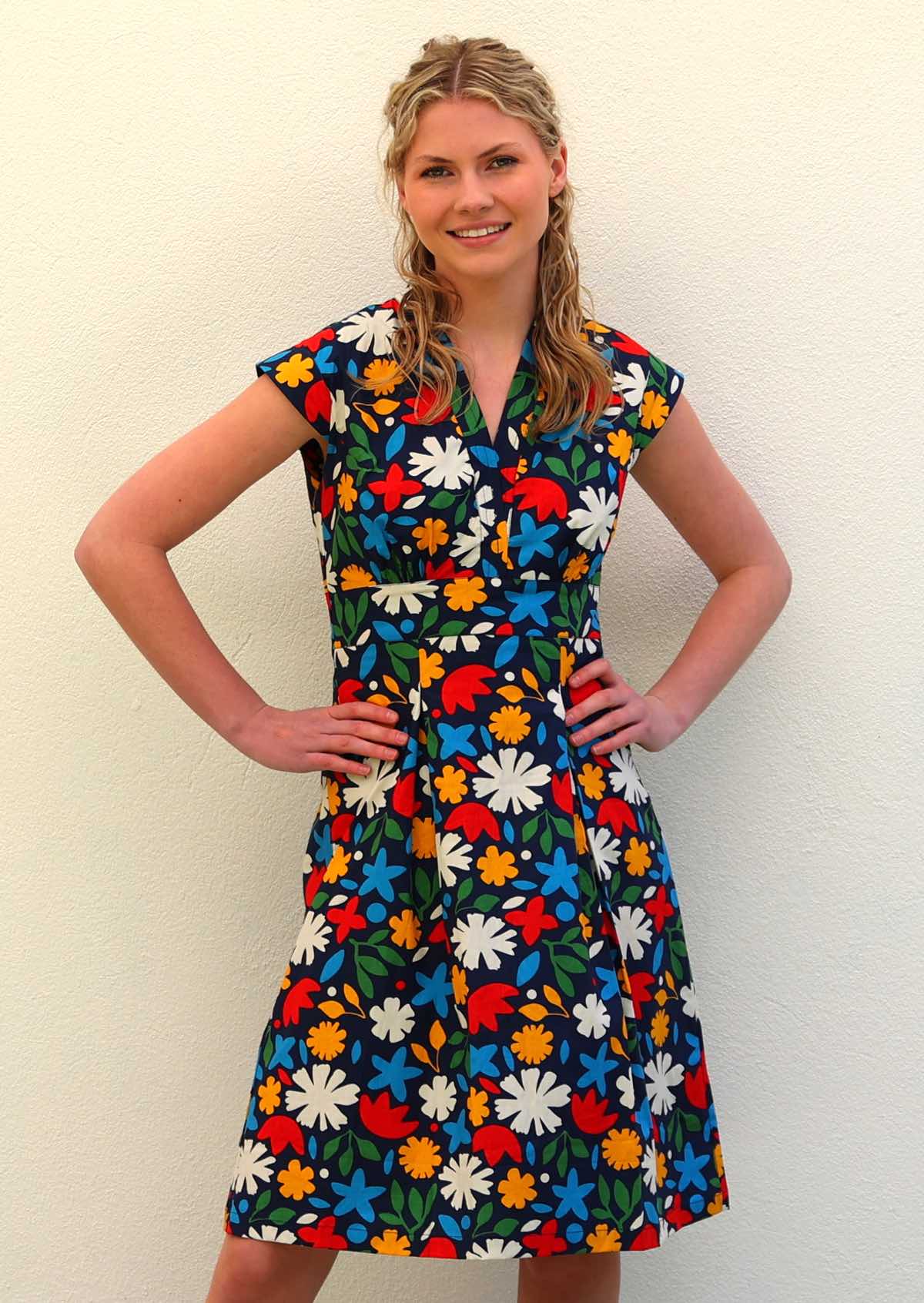 Model standing with hands on hips wearing 100 percent cotton dark navy blue base and bright abstract floral print cotton retro dress