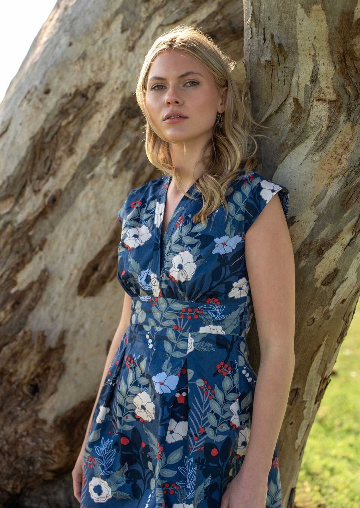 Model leans on tree in retro cotton dress with two box pleats in front and V-neckline