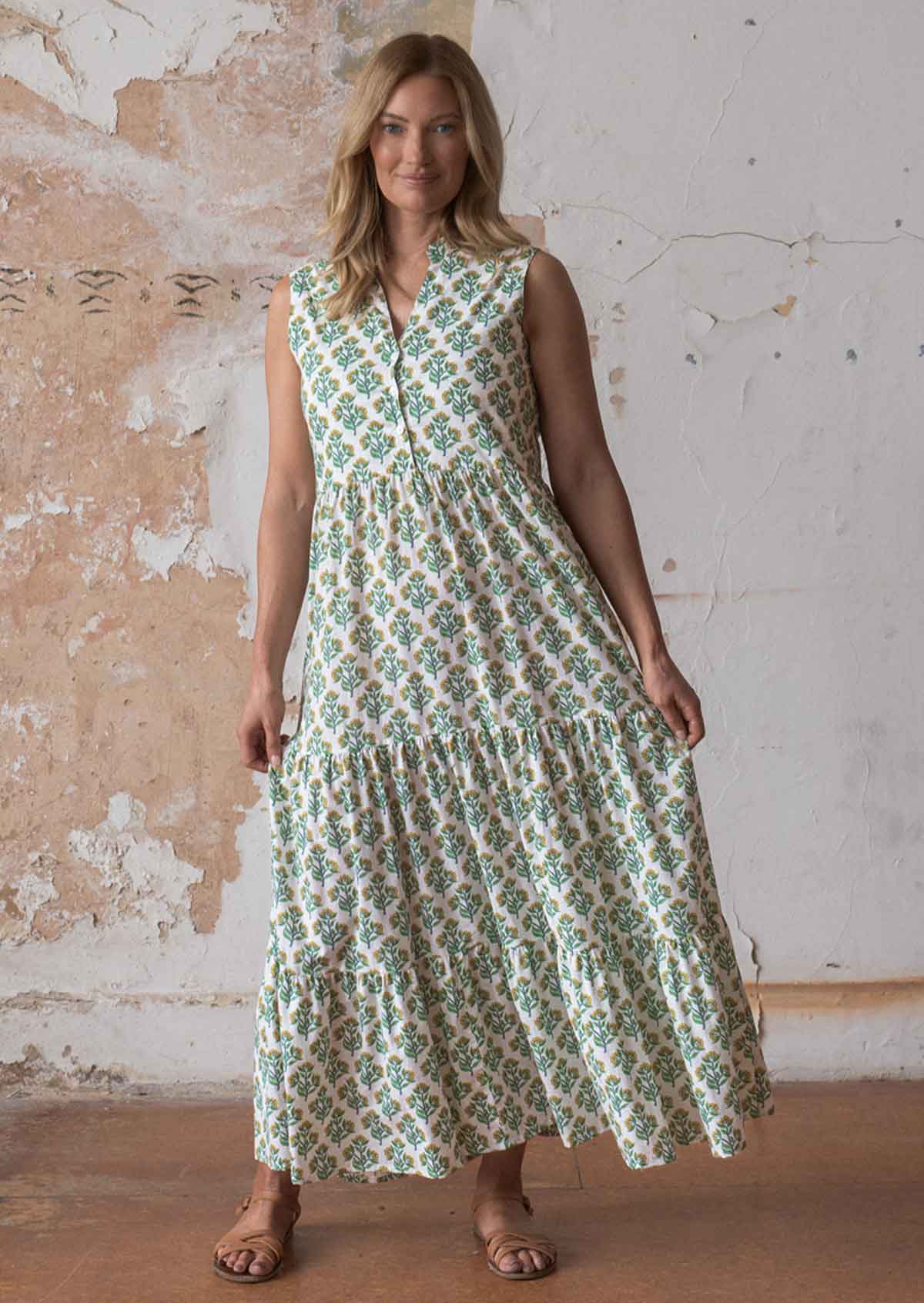 Woman wears cotton sleeveless maxi dress with buttoned bodice and three tiered flowy skirt