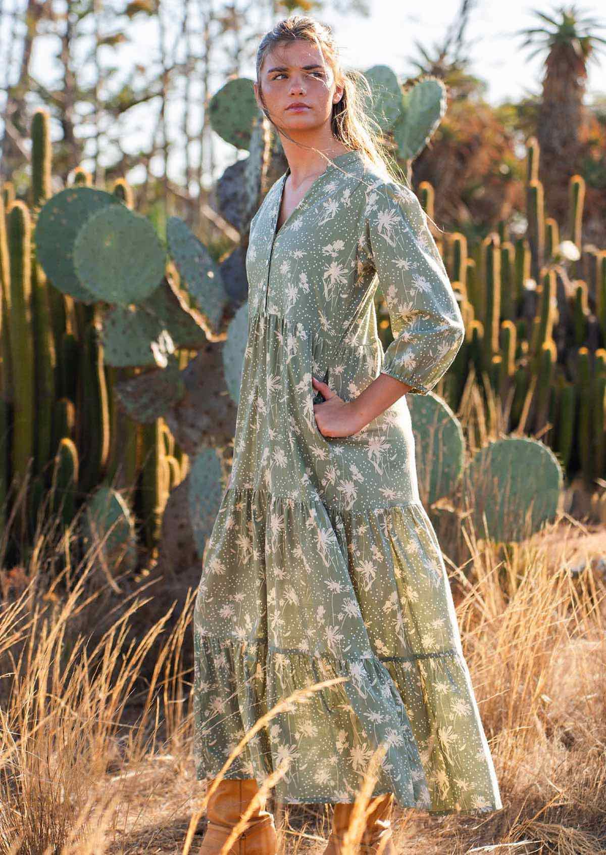 Model stands with hands in pocket of cotton maxi dress in cream floral on a pale green base print