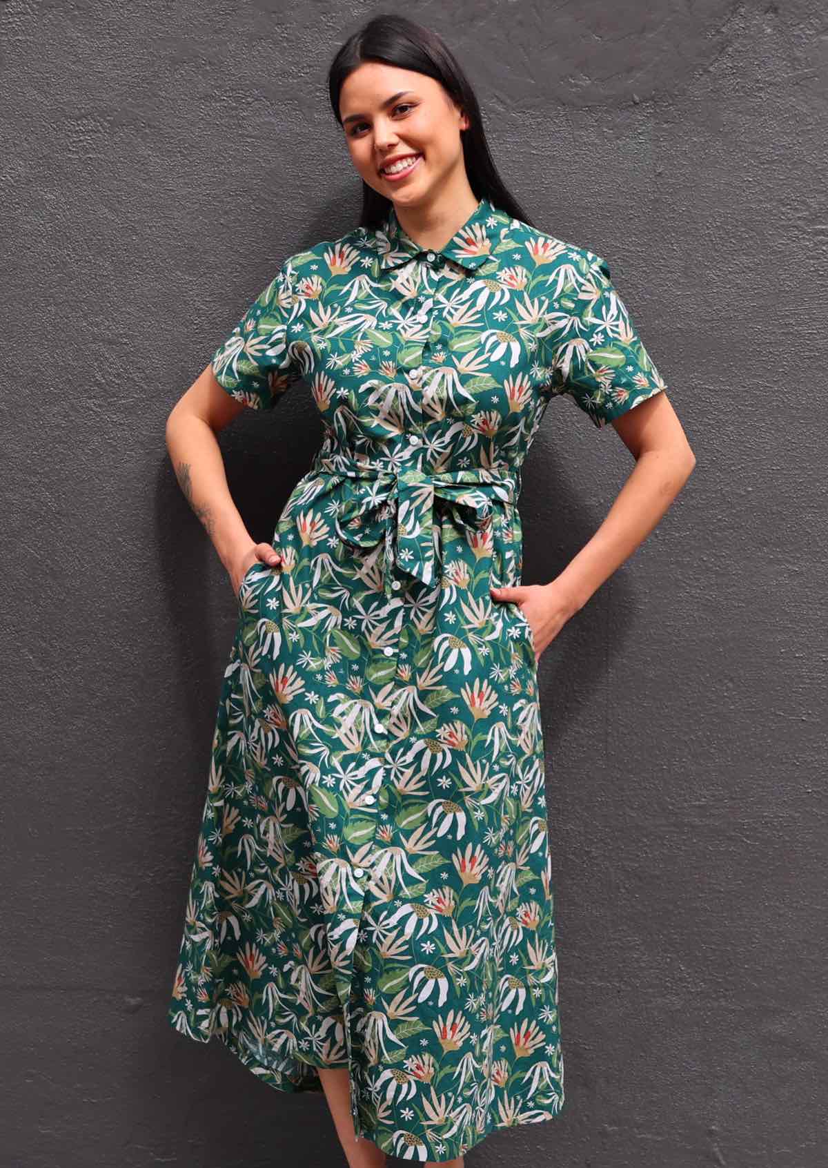 Woman with dark hair wearing 100% cotton green floral shirt dress with hands in pockets 