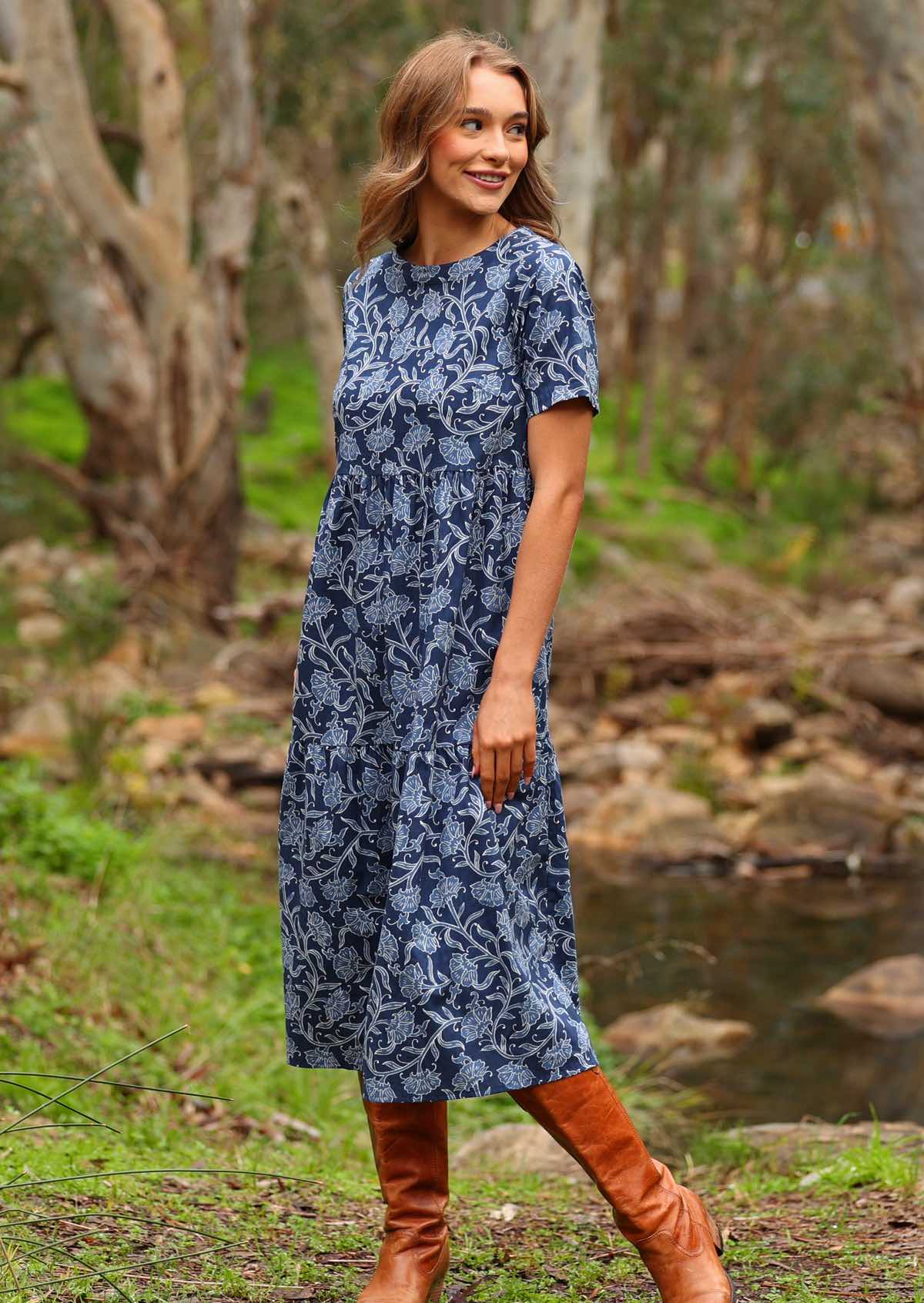 Model standing side on wearing Claudia Dress Neela navy blue 100 percent cotton maxi sundress paired with tan leather boots