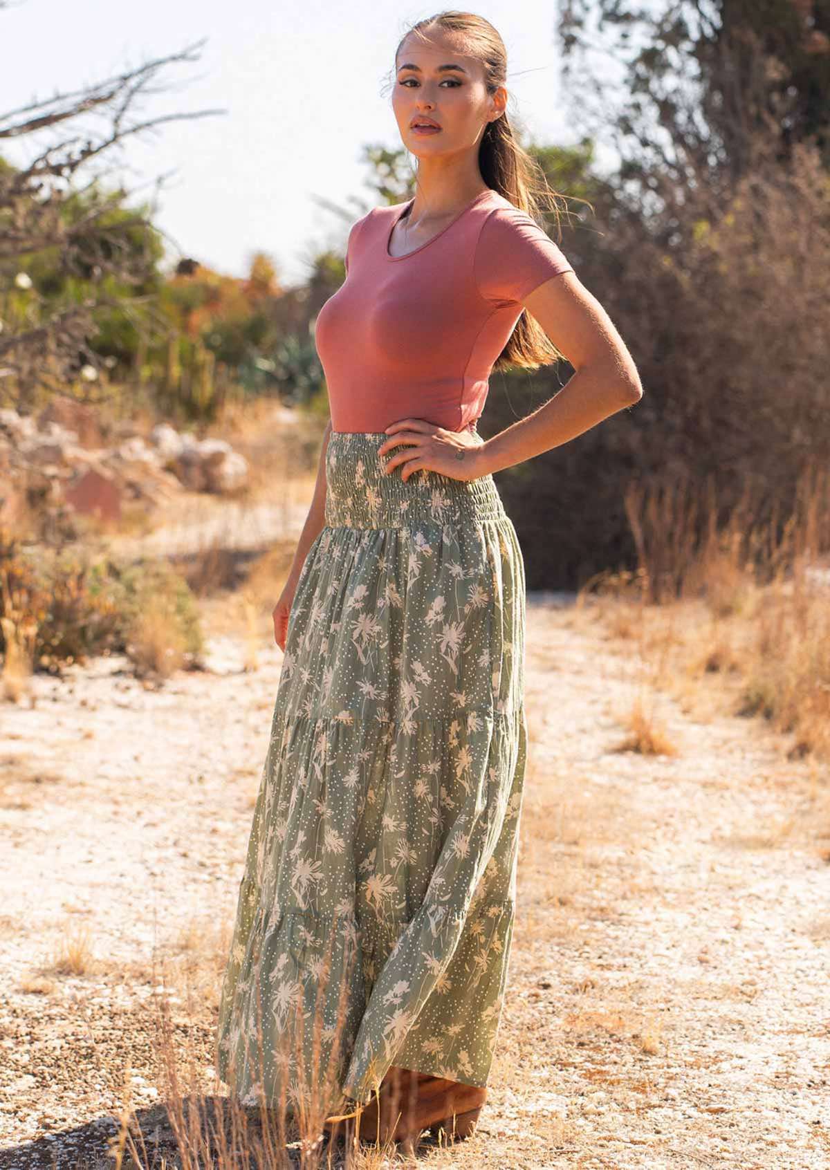 Woman wears cotton maxi skirt with cream floral silhouettes on a pale green base