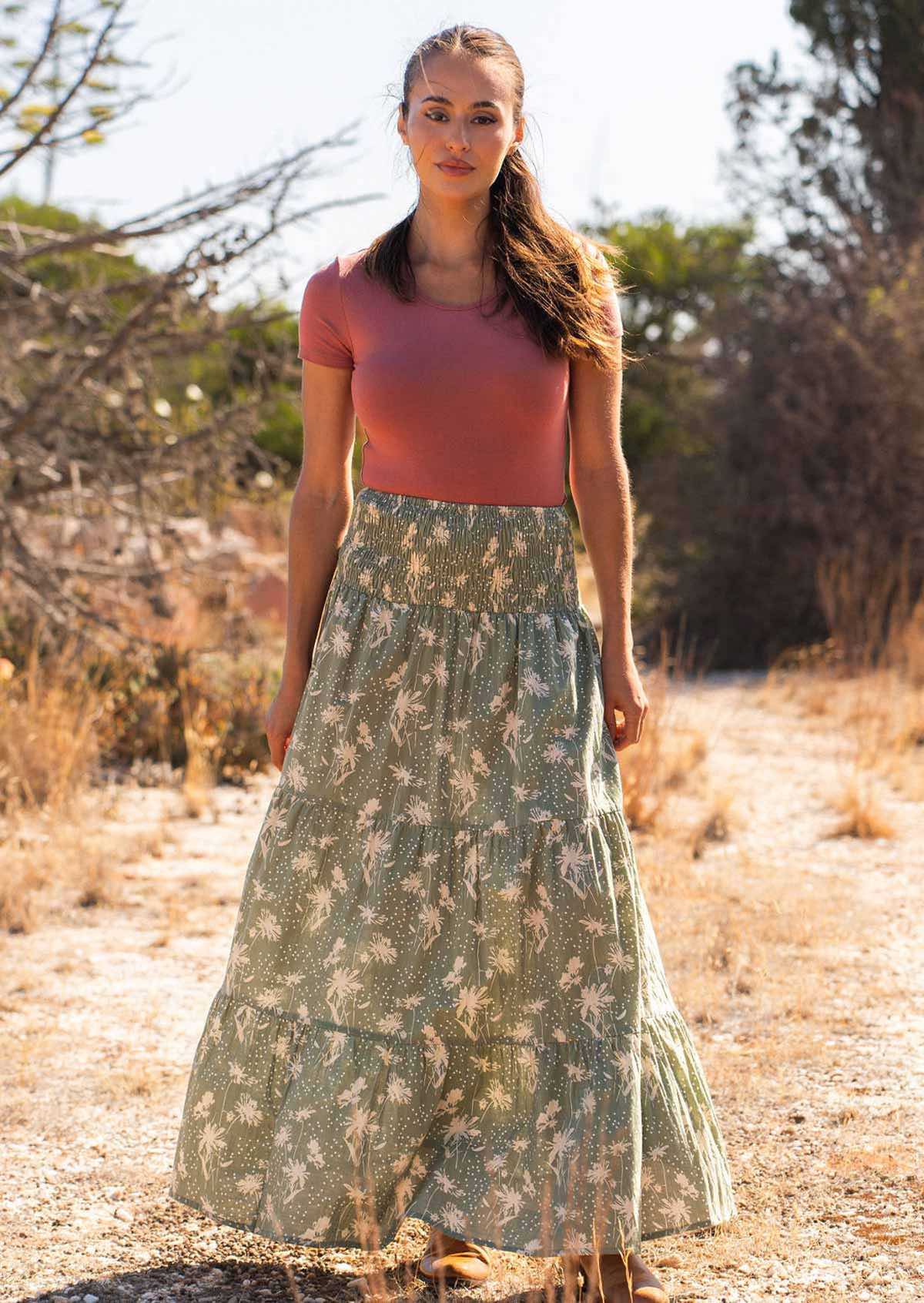 Woman stands in cotton maxi skirt with wide elastic shirred waistband, in pale green and floral print