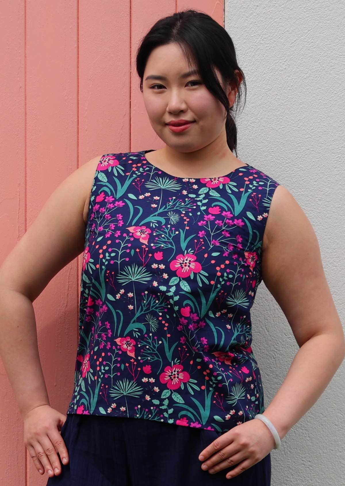 Model with hands on hips wearing 100 percent cotton pink and purple floral on dark blue base sleeveless top
