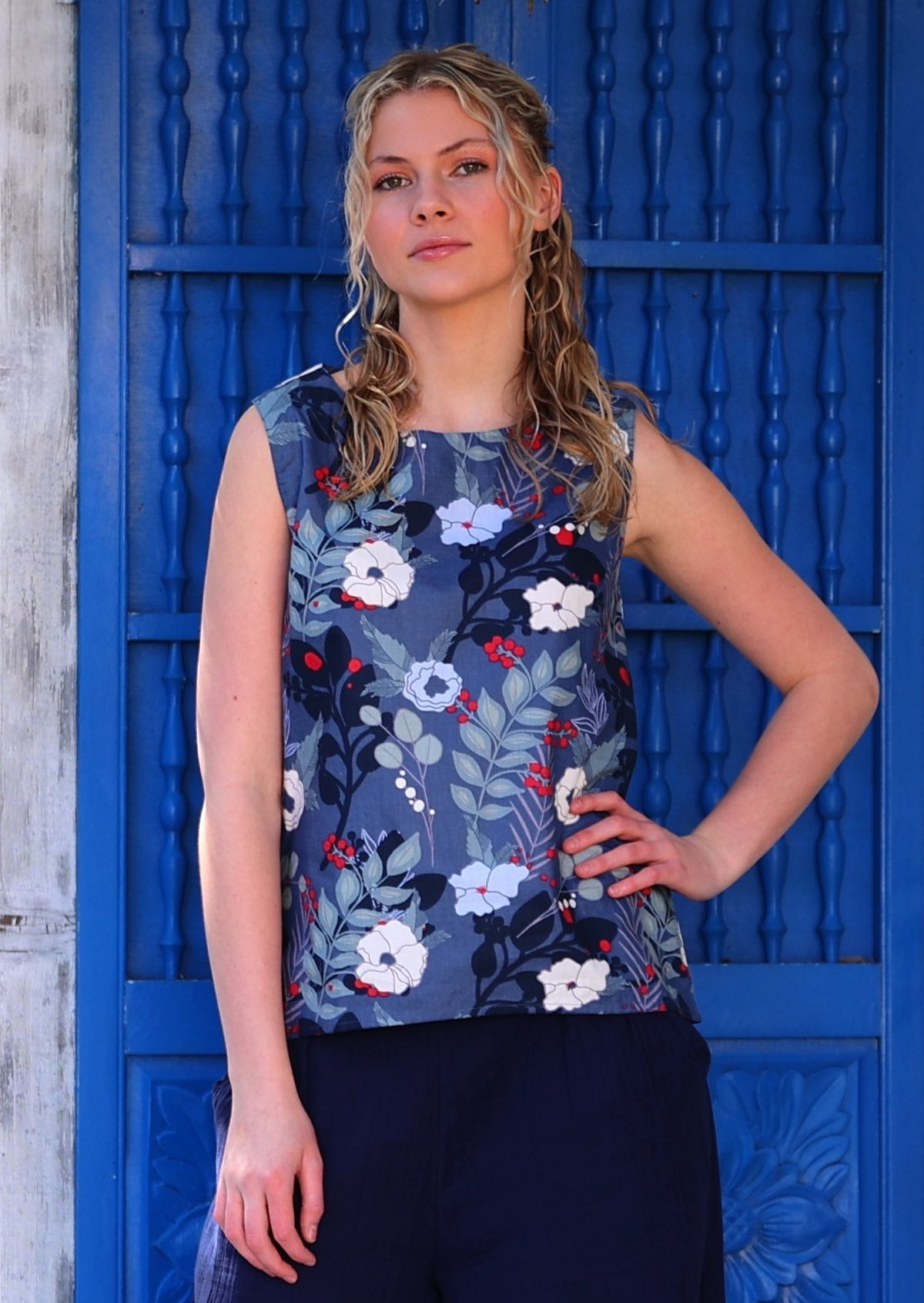 Model standing in front of blue door with hand on hip wearing 100 percent cotton navy blue floral sleeveless top