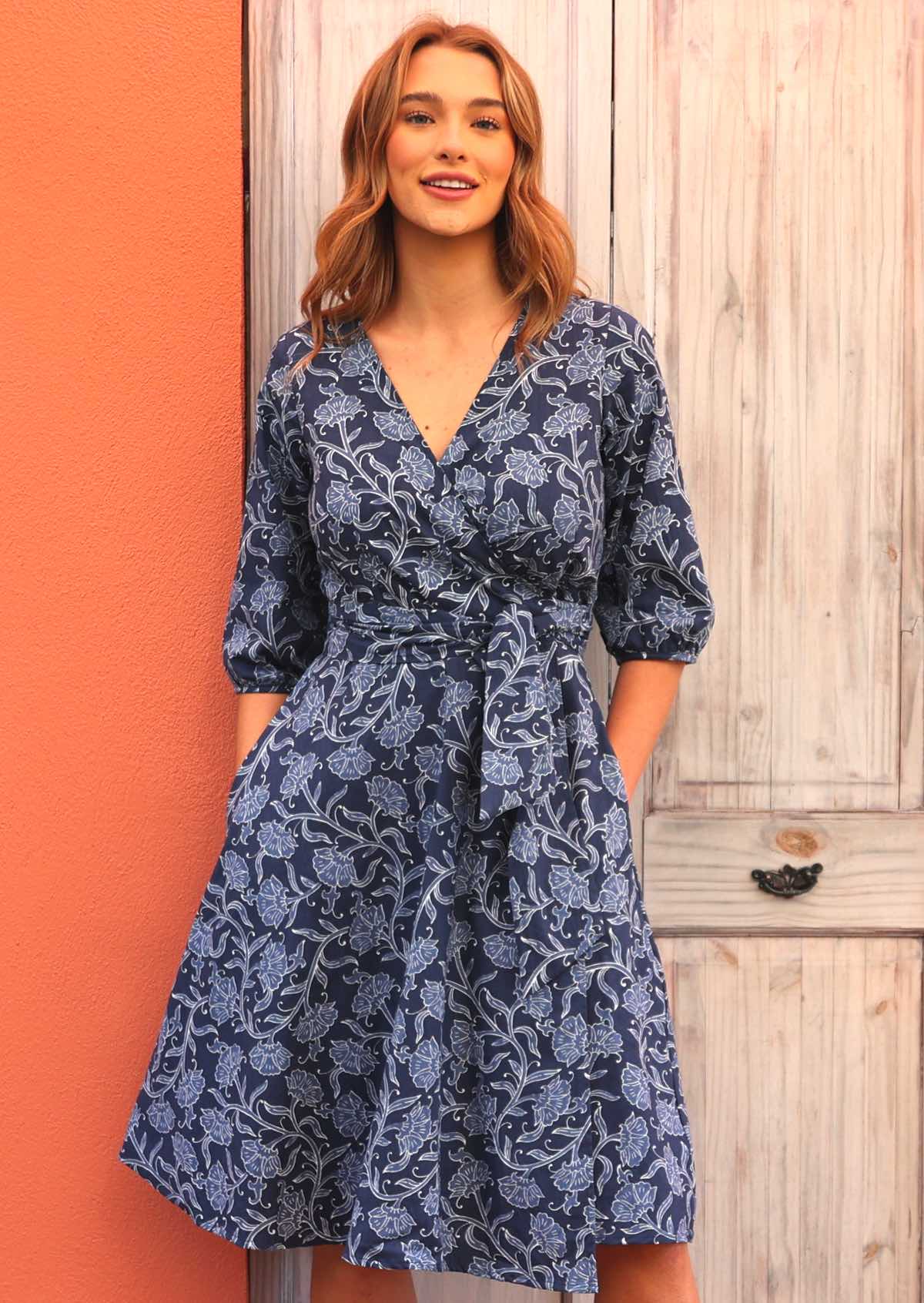 Model standing wearing Ella Wrap Dress Neela 100 percent cotton navy blue floral wrap dress 3/4 sleeves with hands in pockets