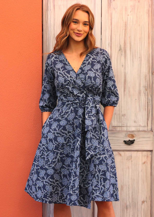 Model standing in front of door wearing Ella Wrap Dress Neela 100 percent cotton 3/4 sleeve navy blue floral wrap dress with hands in pockets