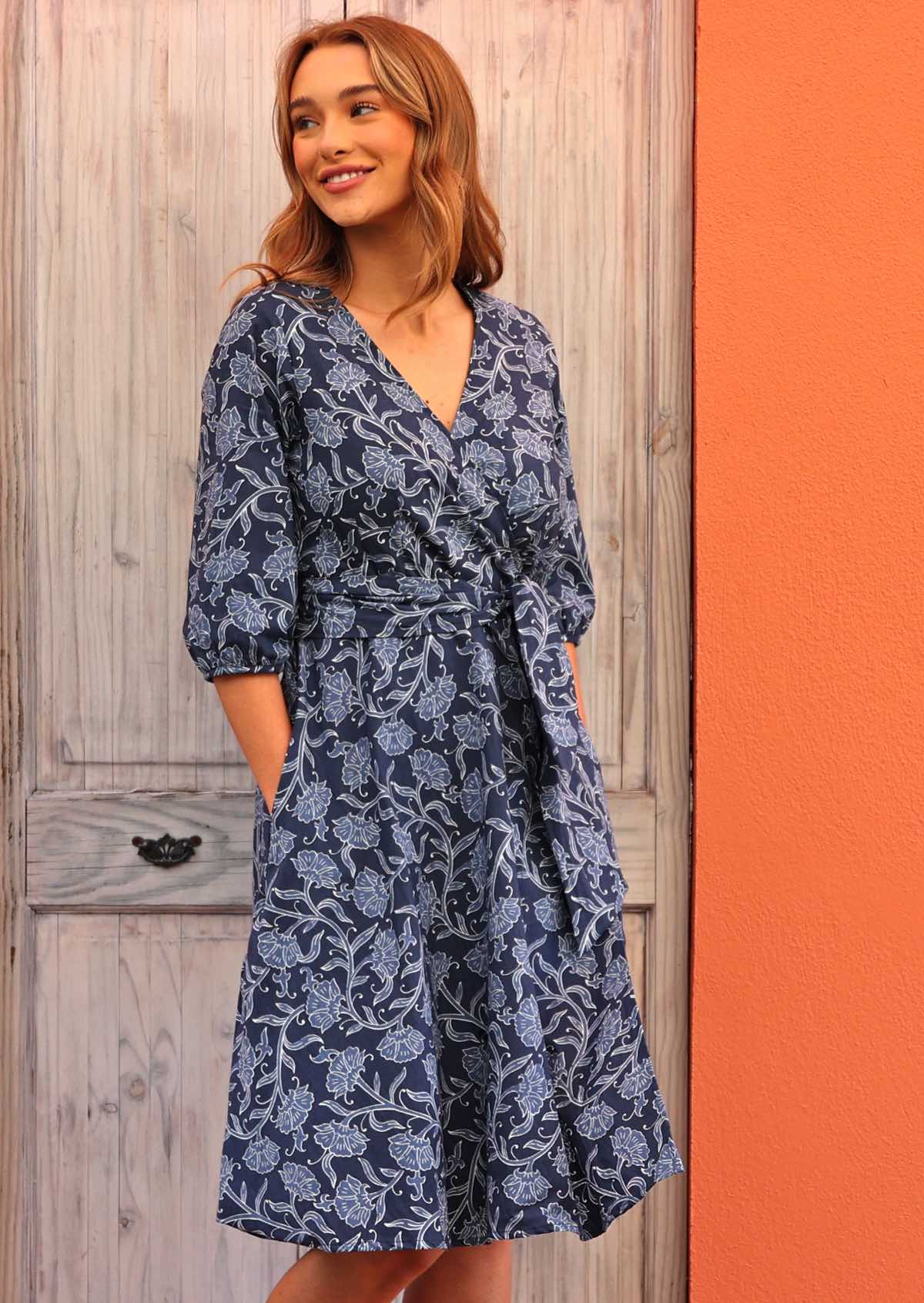 Model standing side on wearing Ella Wrap Dress Neela 100 percent cotton navy blue floral wrap dress with hands in pockets