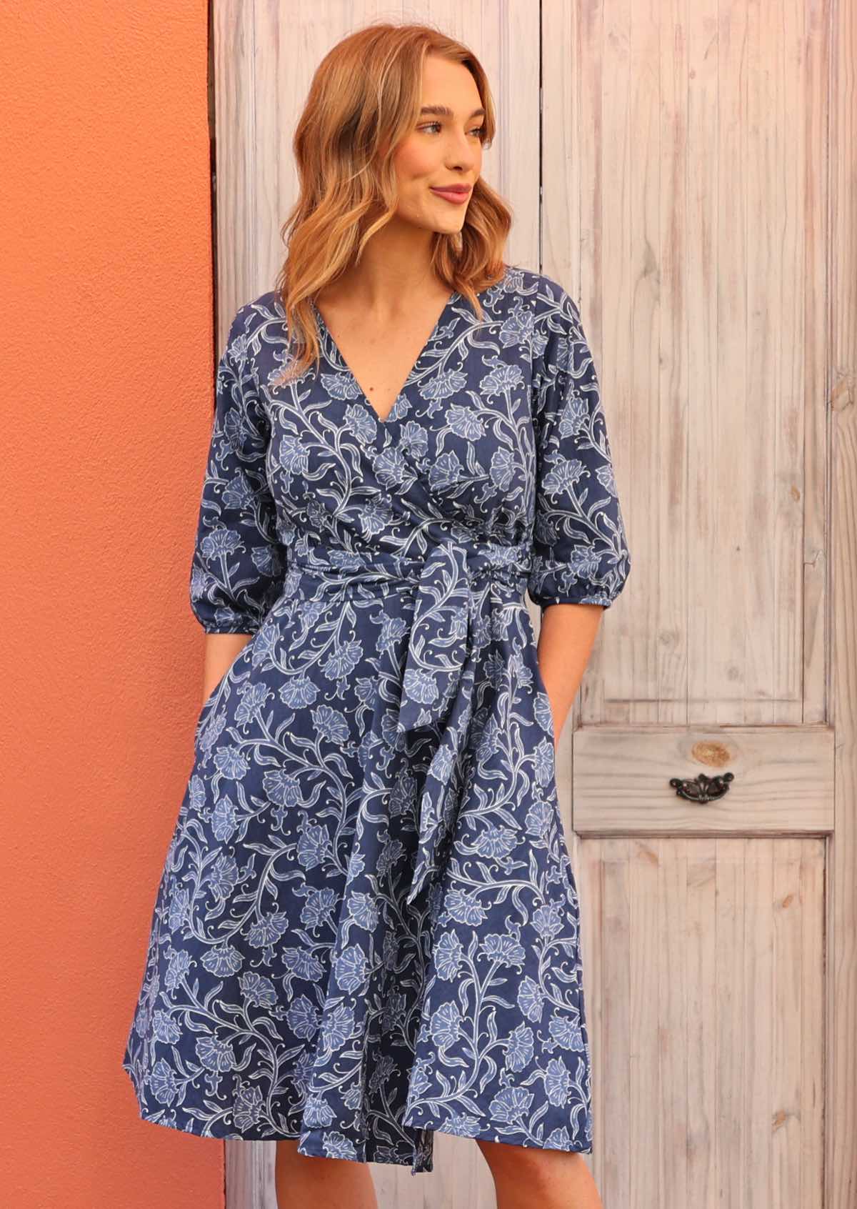 Model standing looking to the side wearing Ella Wrap Dress Neela 100 percent cotton navy blue floral wrap dress with hands in pockets 