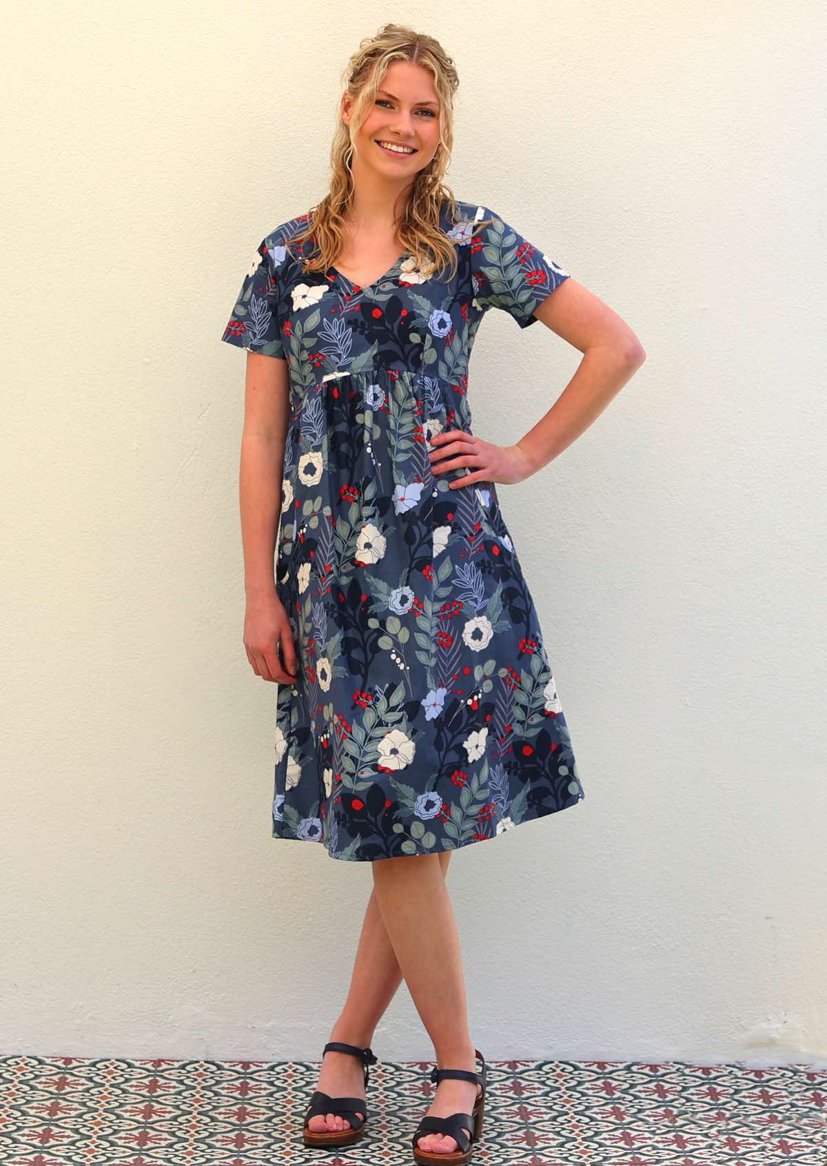 Woman wears cotton knee length dress with empire waistline in bold blue floral print