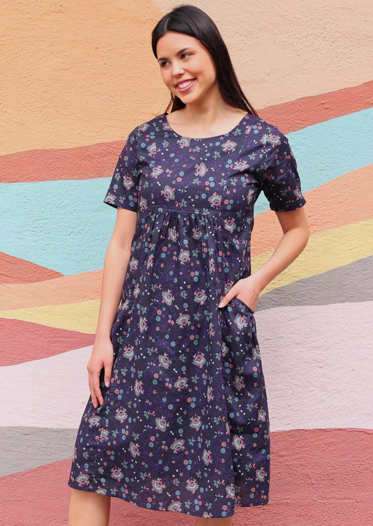 Woman wearing Indian print cotton dress with pockets in front of sun mural