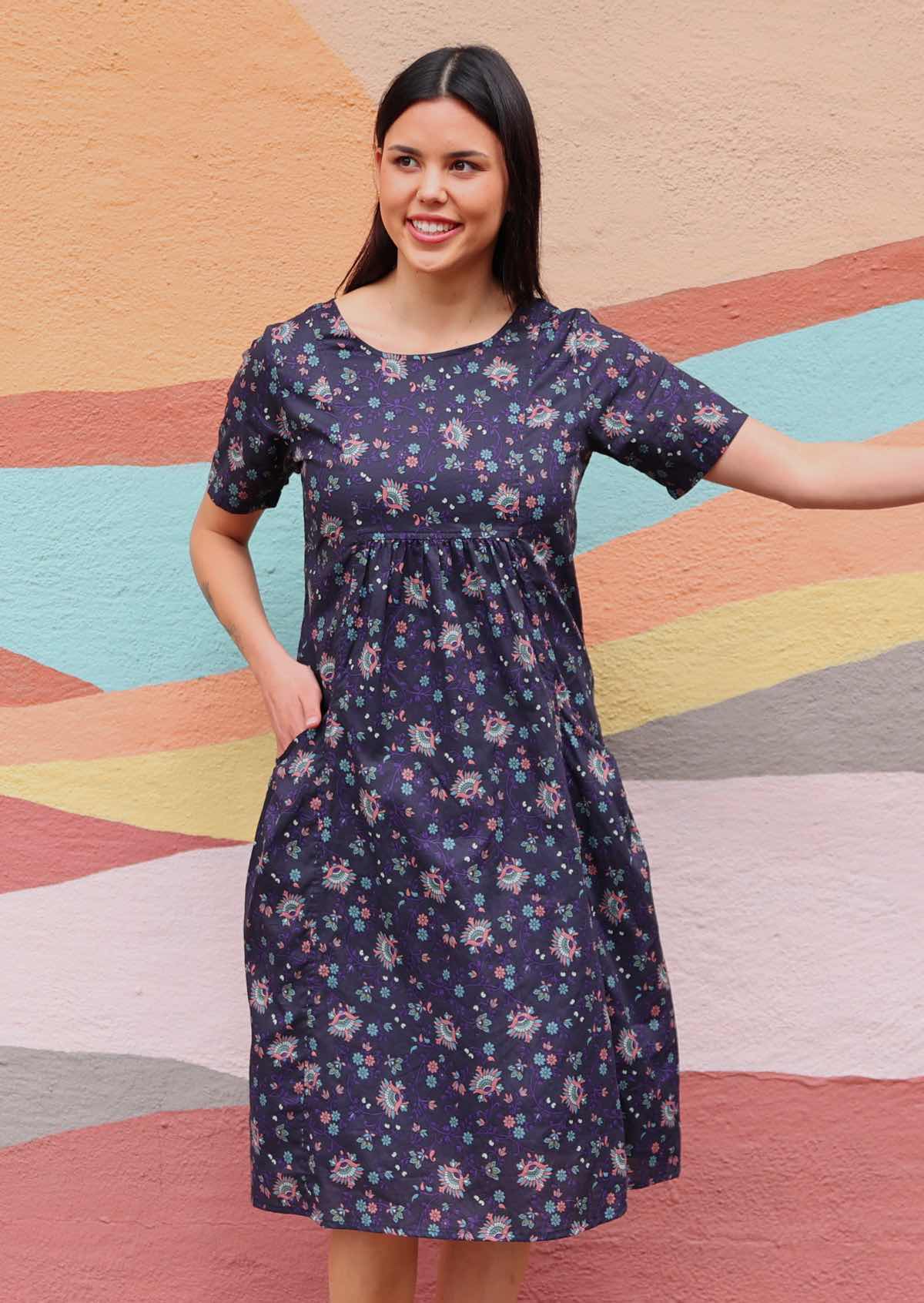 Woman wearing Indian print cotton dress with hand in pocket in front of sun mural