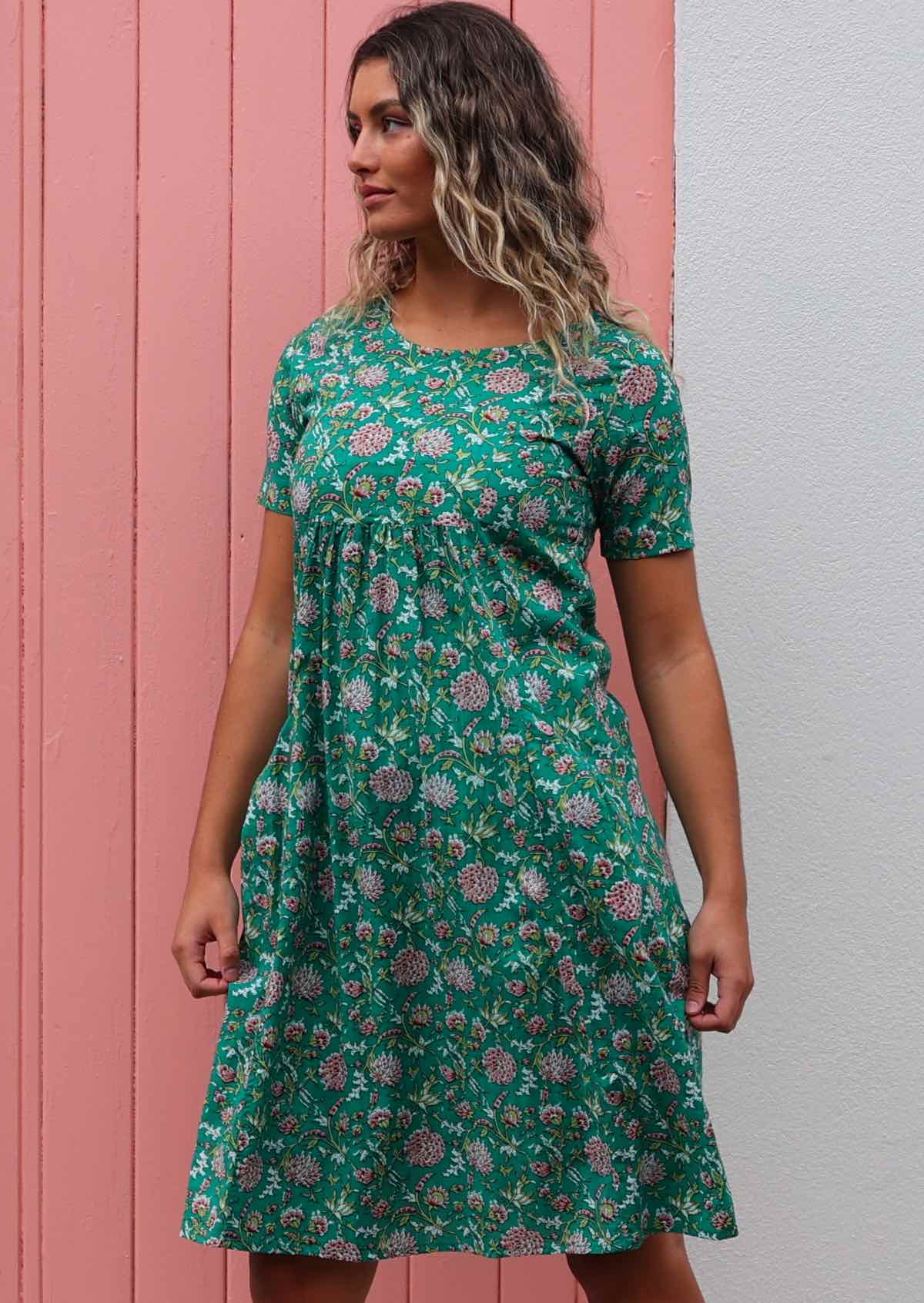 Model standing in front of pink door wearing 100 percent cotton green floral sundress