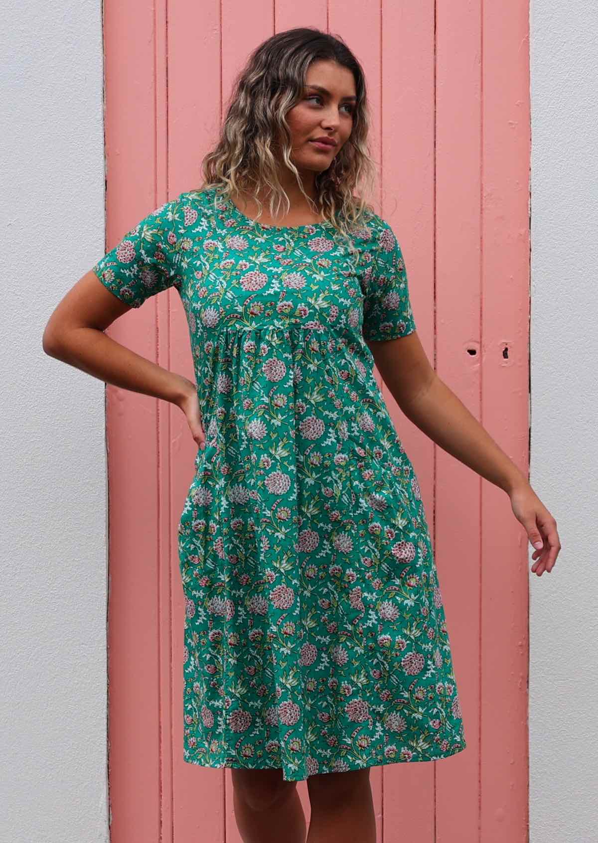 Model standing in front of pink door wearing one hundred percent cotton green floral sundress