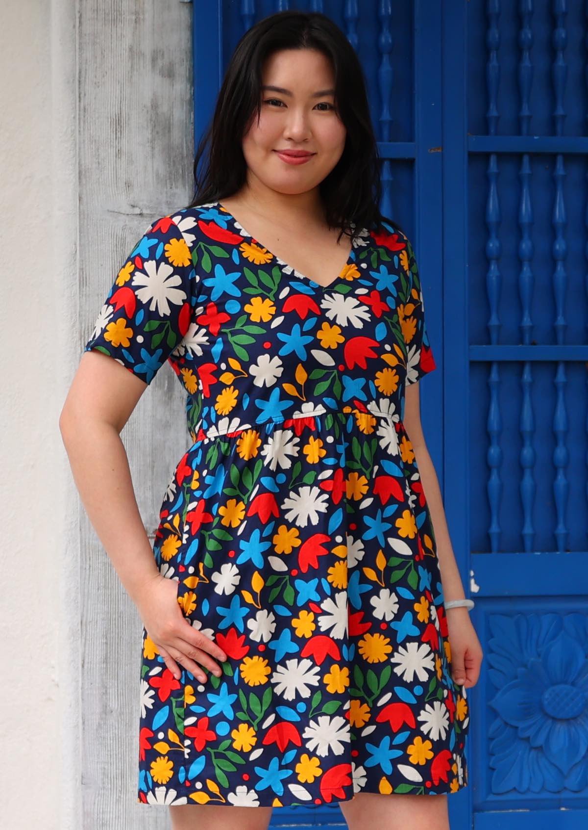 Model poses in cotton above knee dress in fun bold floral print on dark blue base with hand in side pocket