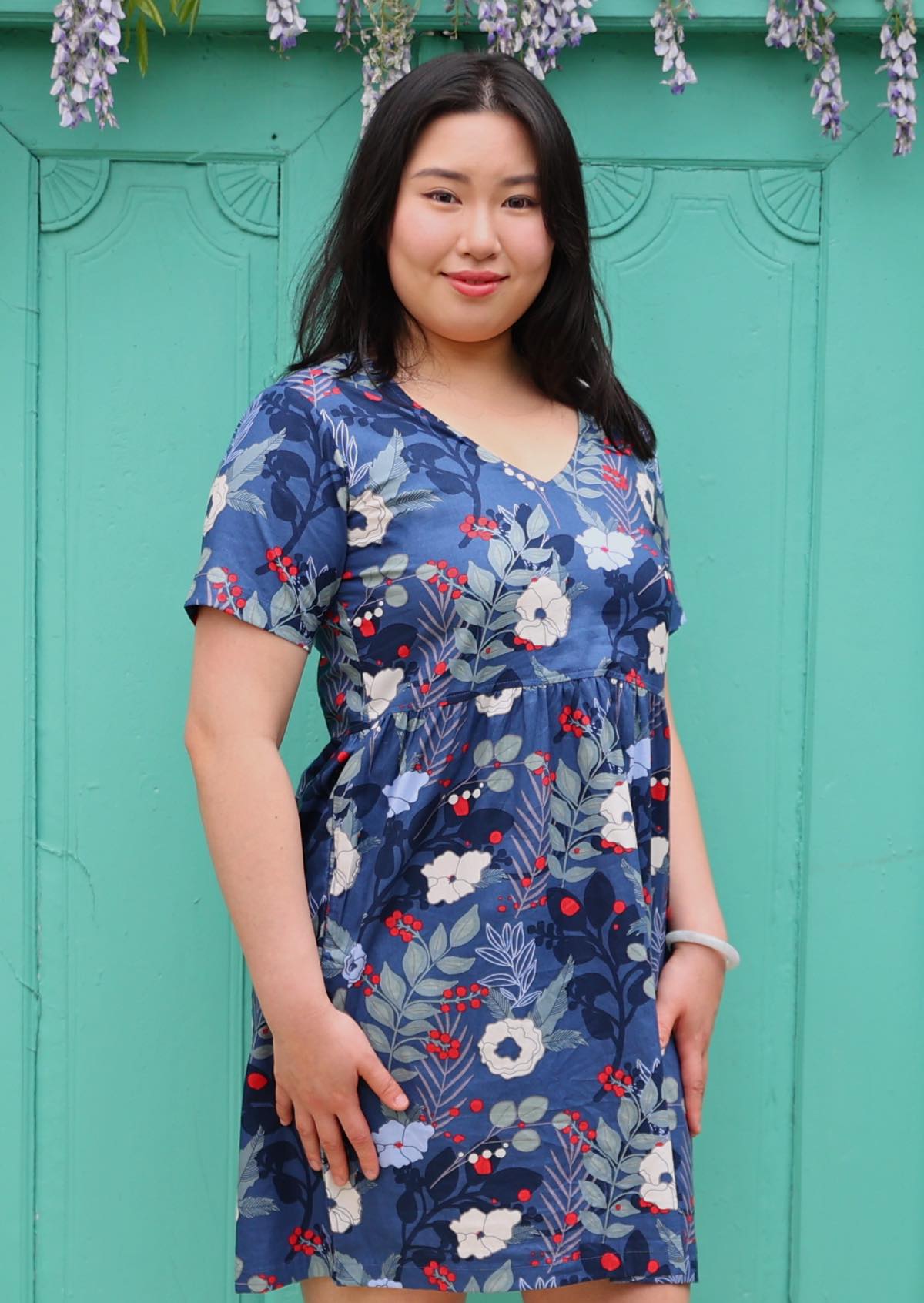 Woman poses in old blue floral print with pops of red cotton short sleeve dress with V-neckline