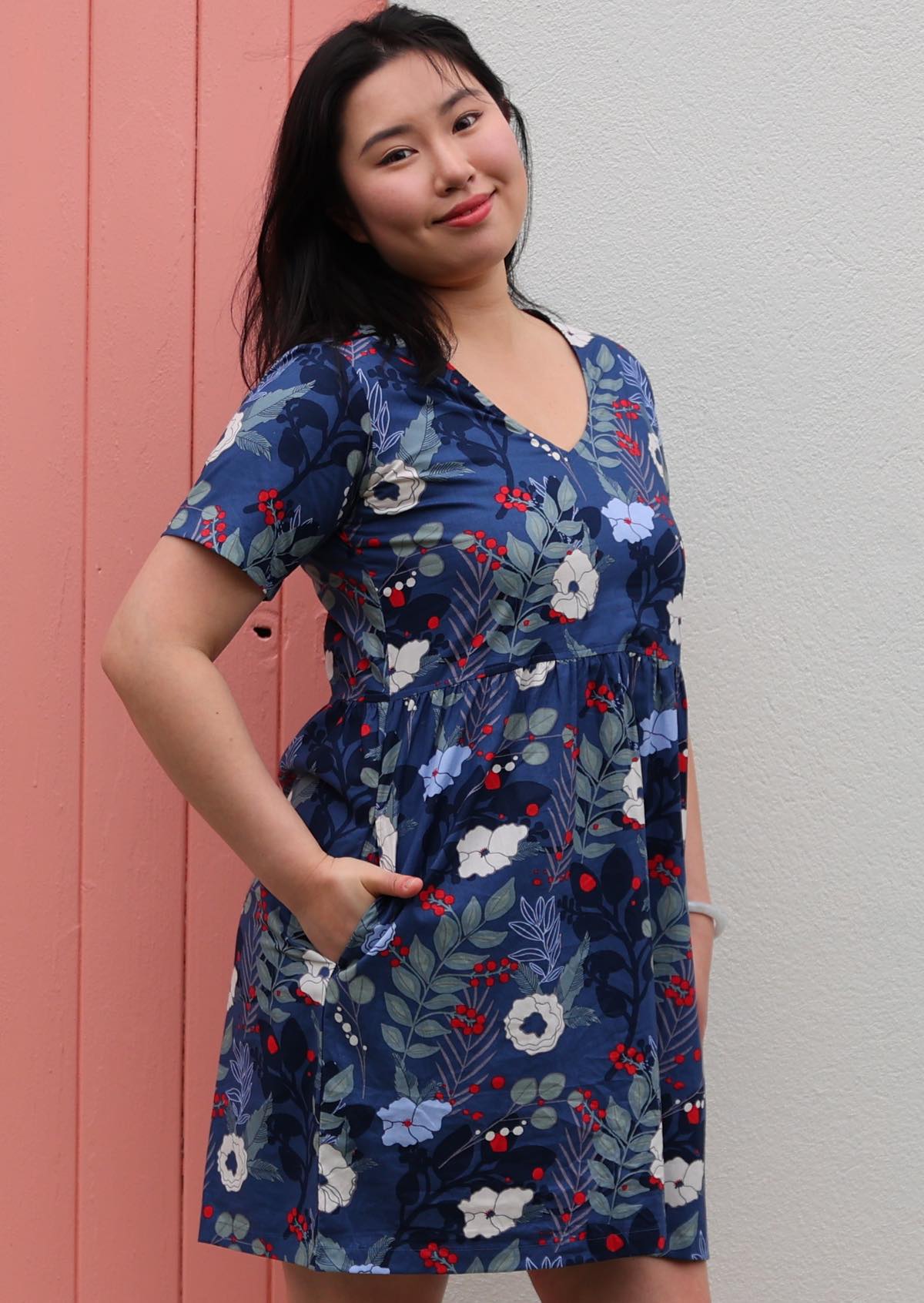 Model poses in above knee cotton relaxed fit dress with V-neckline and pockets in blue floral print