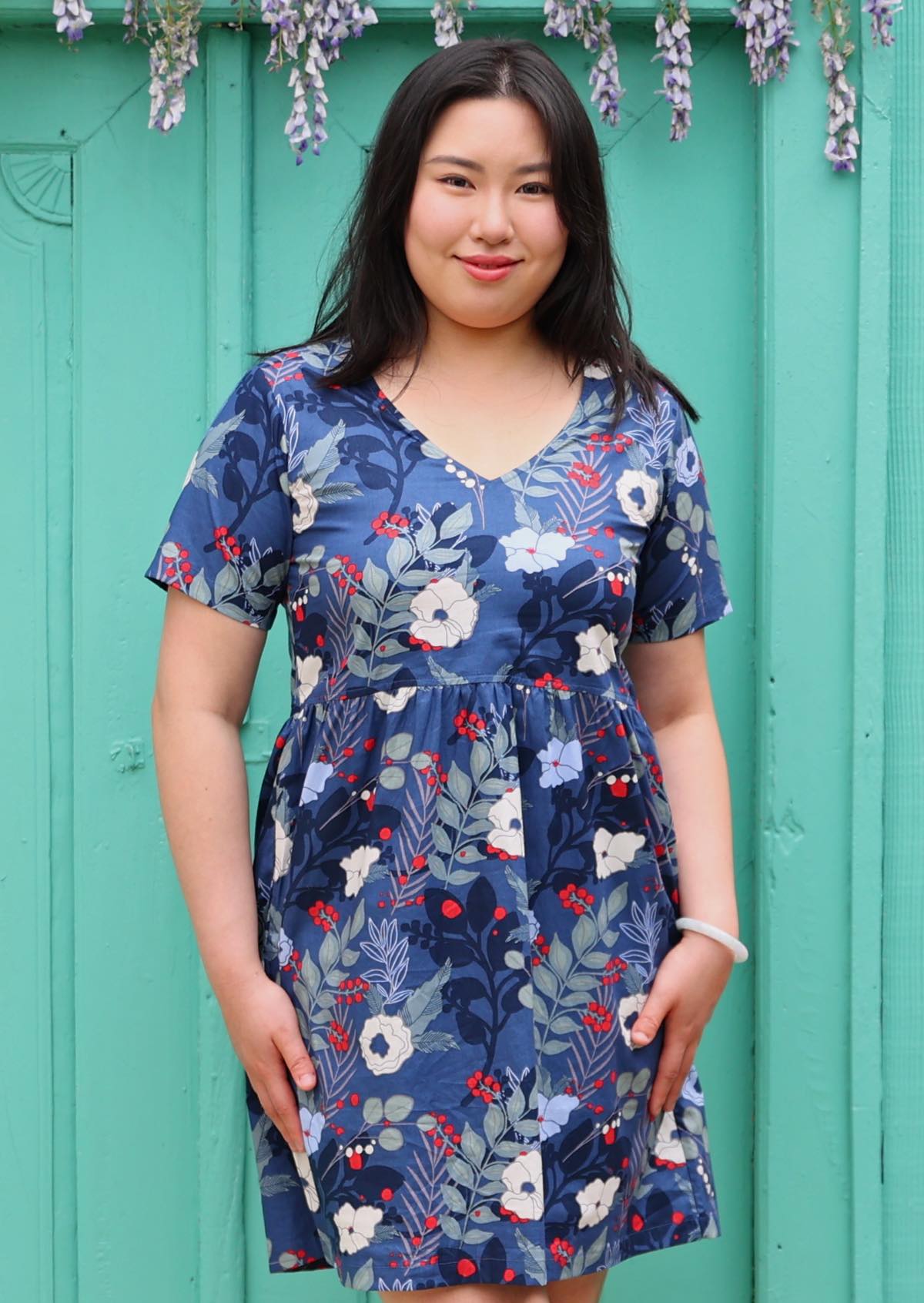 Model wears bold blue floral print cotton above knee dress with short sleeves and v-neckline