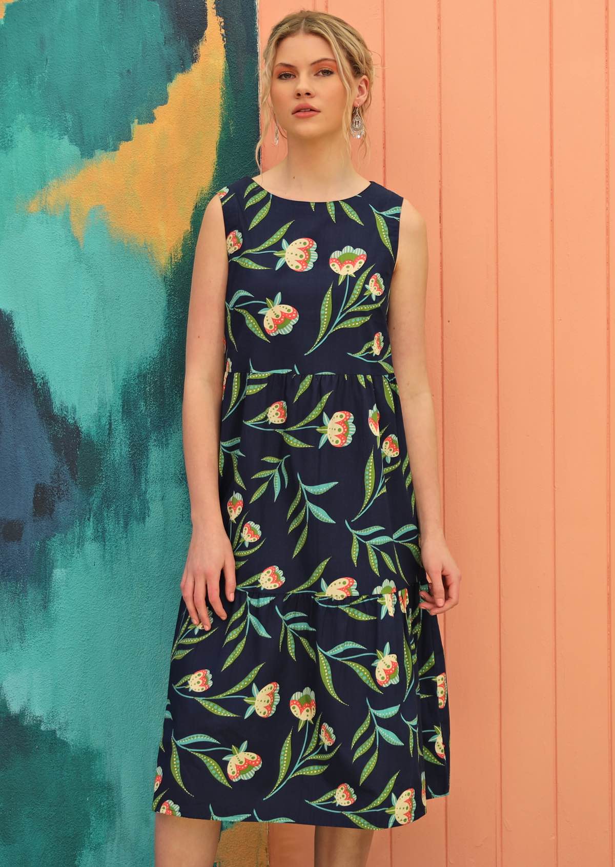 Model wears floral print dress on a navy base. 