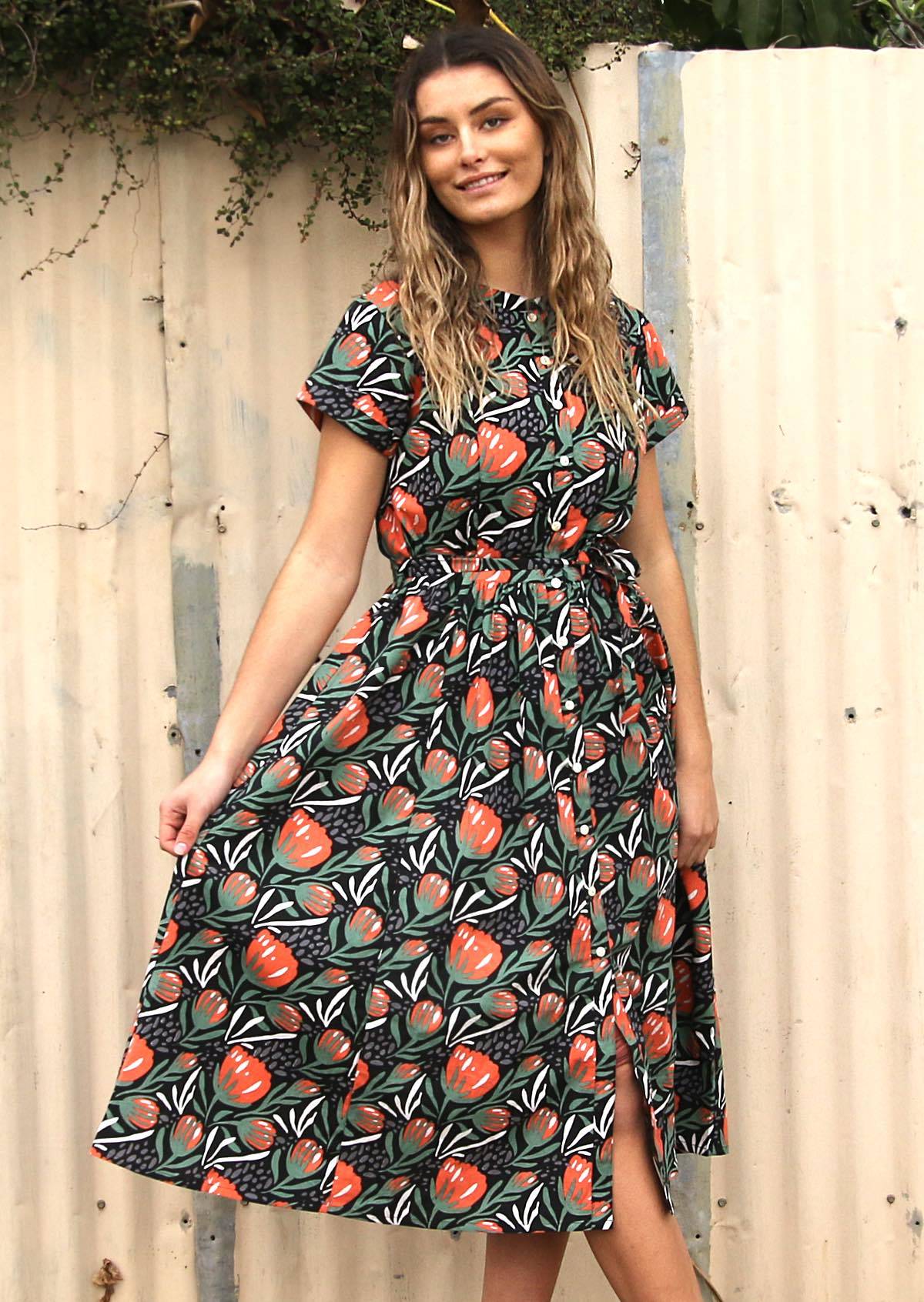 Woman with long hair standing in front of fence wearing button through cotton shirt dress in black 