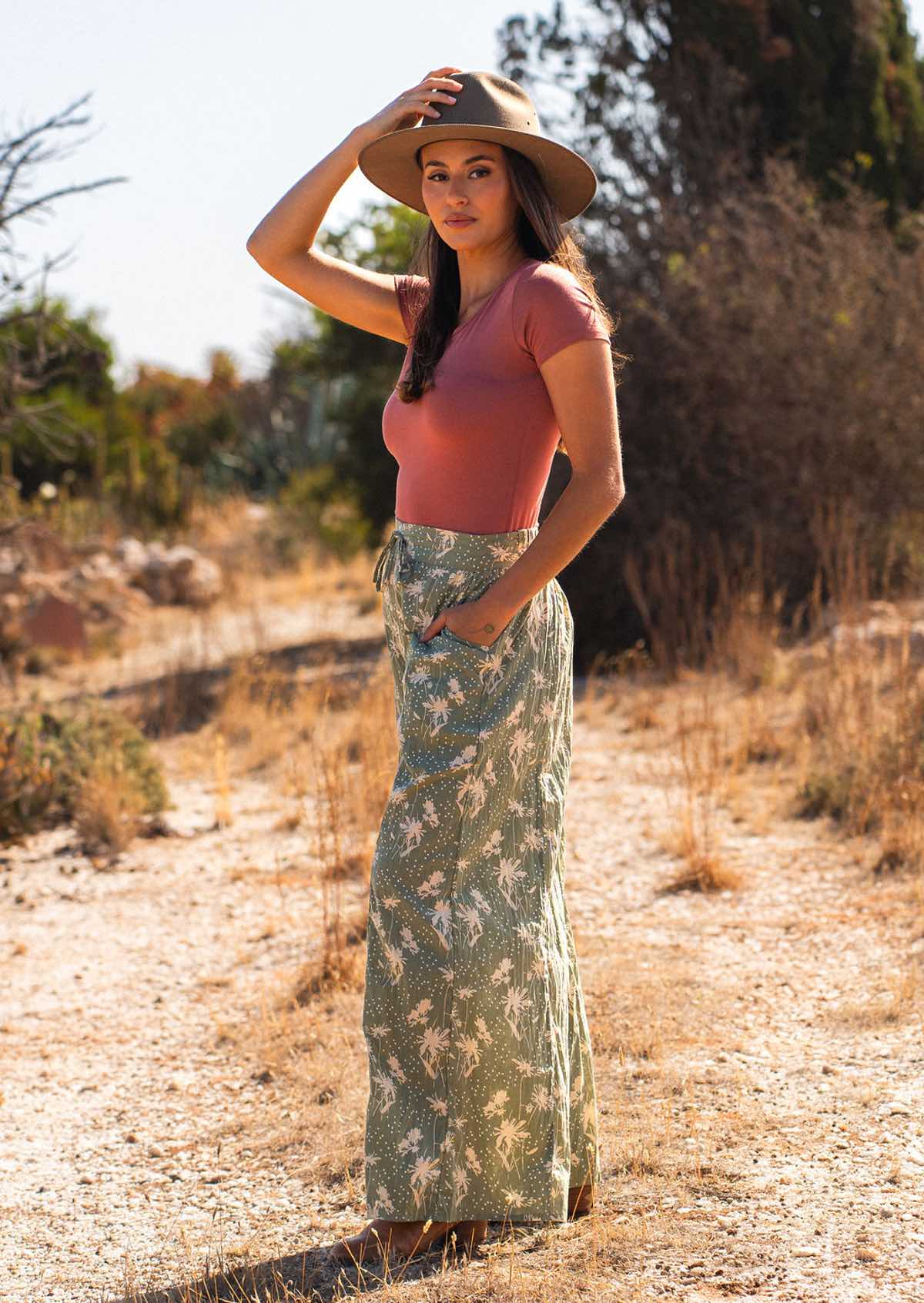 Woman stand sideways in cotton wide leg pants in pale green with cream floral silhouette print