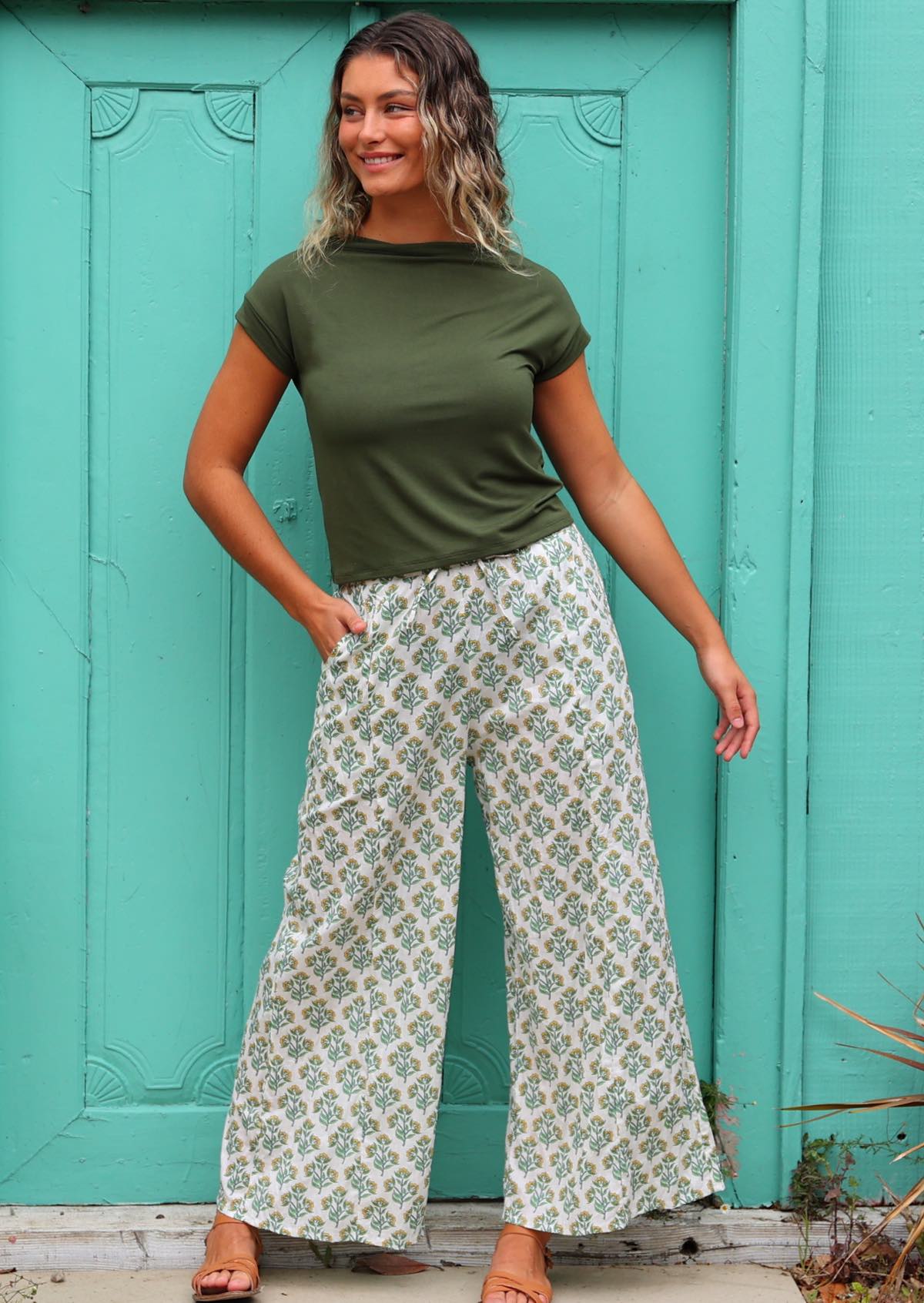 woman wearing white cotton palazzo pant with floral detail in front of aqua door