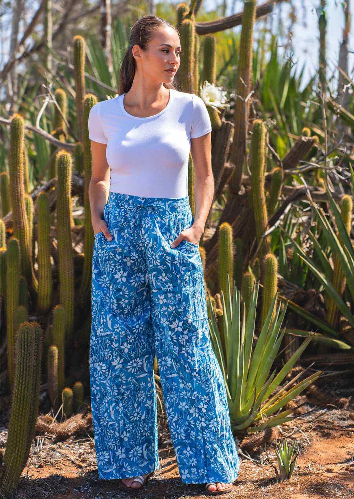 Woman stands in front of cactuses in cotton wide leg pants in blue floral print, with her hands in the pockets