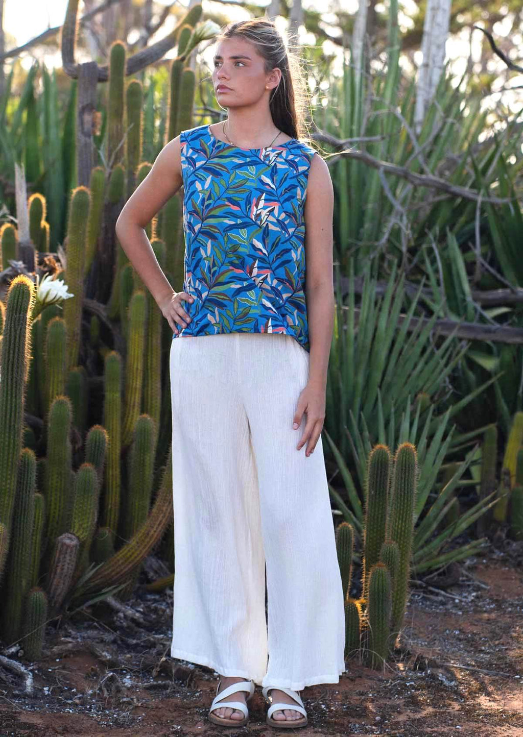 woman wearing wide legged white cotton pants and blue cotton top in front of cacti 