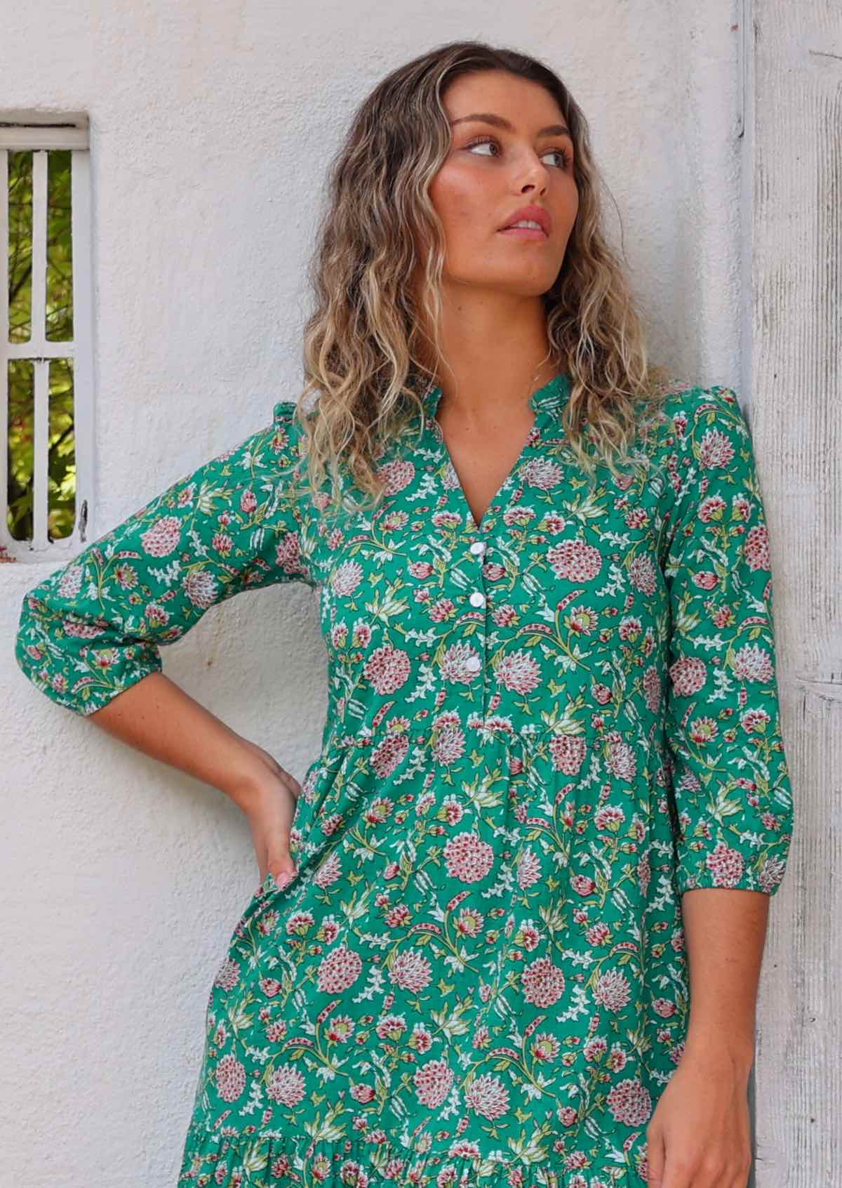 Close up of model looking up and standing in front of white wall with one hand on hip wearing long sleeved 100 percent cotton maxi dress