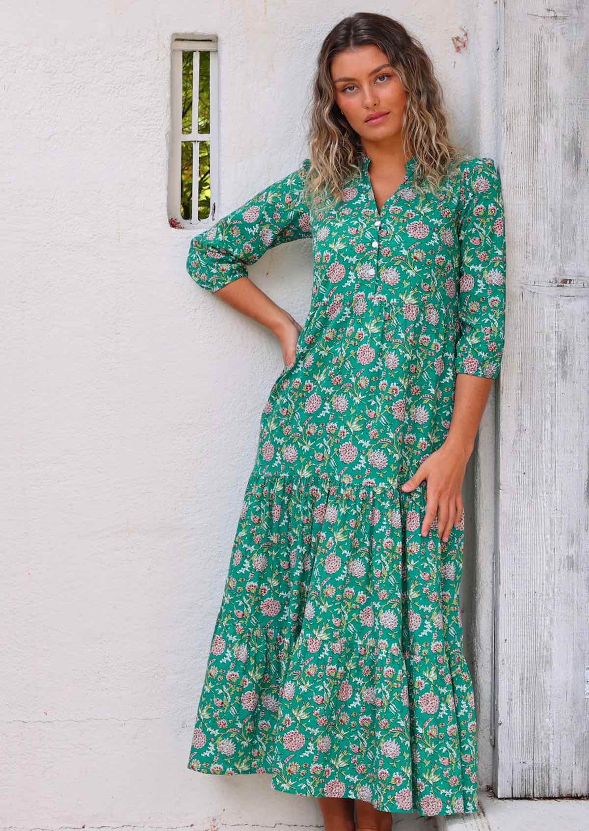 Model standing in front of white wall and against wooden frame with one hand on hip wearing long sleeved 100 percent cotton maxi dress