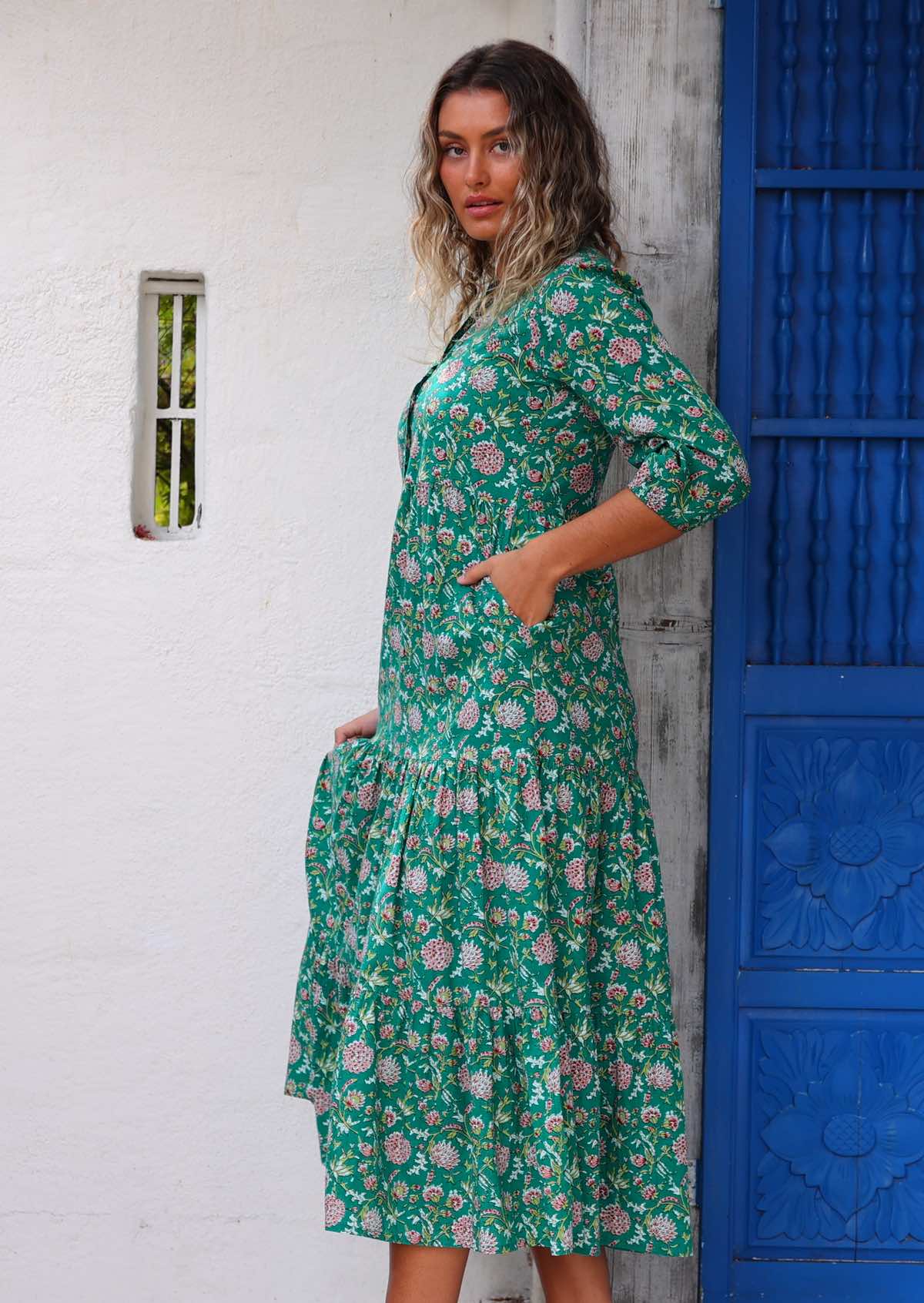 Model standing side on in front of white wall with one hand in pocket wearing long sleeved 100 percent cotton maxi dress